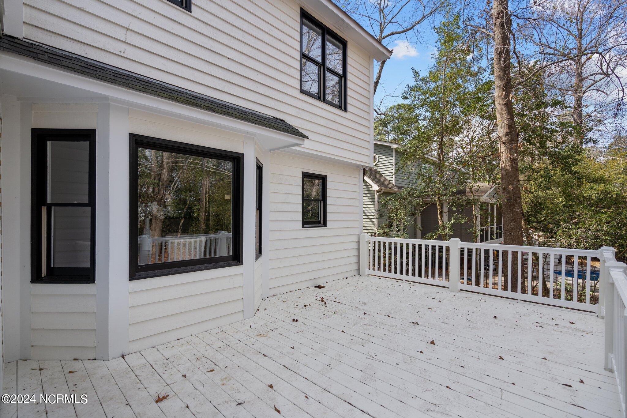 White-painted deck beside a white-sided house, with black-trimmed windows and trees beyond the railing.