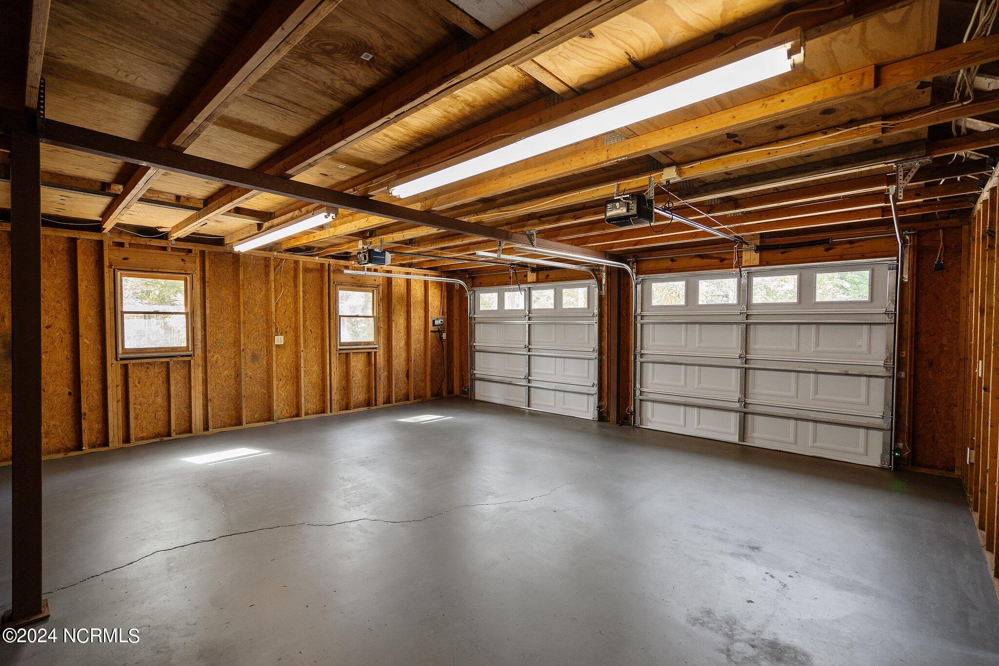 Empty two-car garage with exposed wooden framing and two white overhead doors.