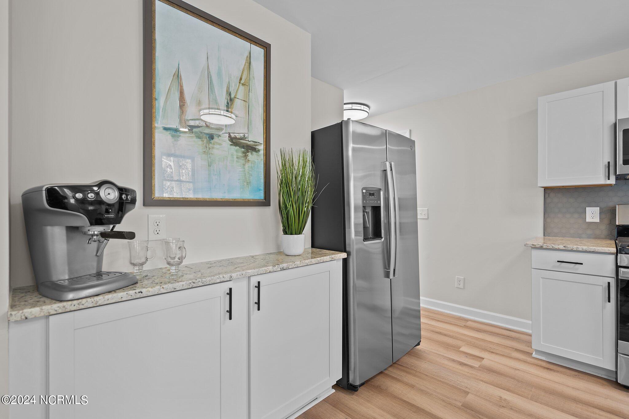 Kitchen with white cabinets, granite counters, stainless steel refrigerator, and a countertop espresso machine.
