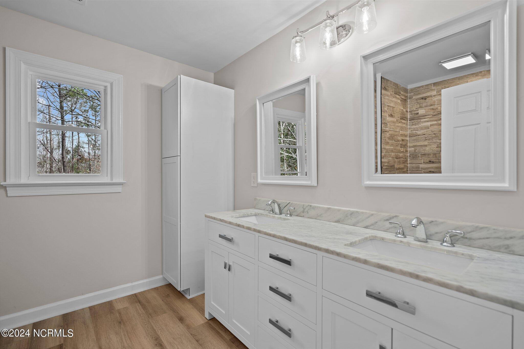 Bathroom with a white double-sink vanity, marble countertop, large mirrors, and wood-look flooring.