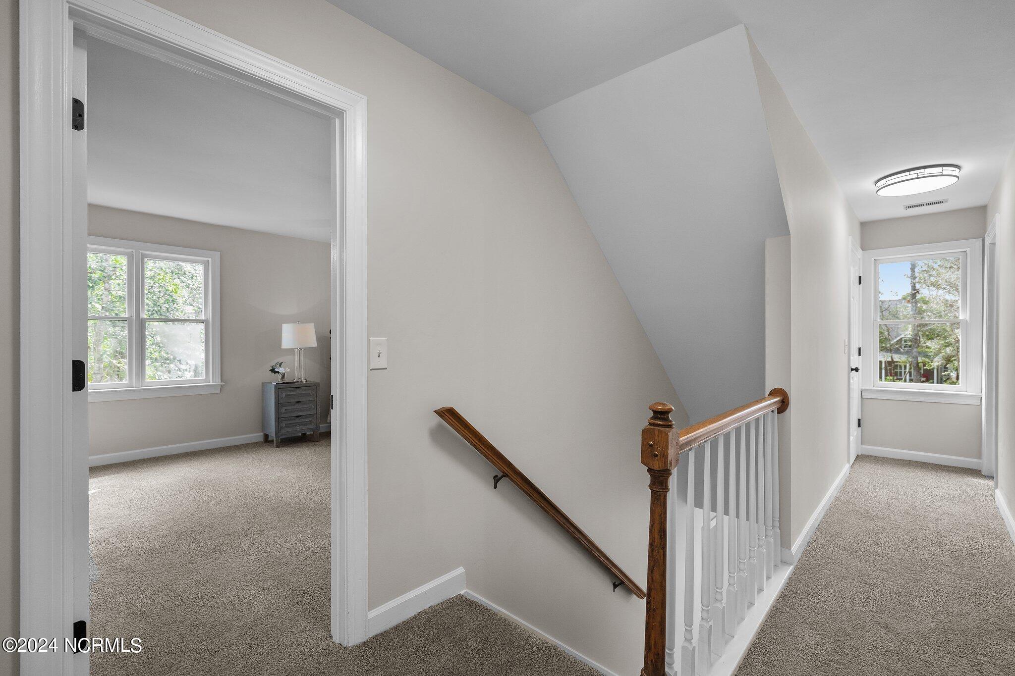 Carpeted upstairs landing with a wooden stair rail and a view into a bedroom.