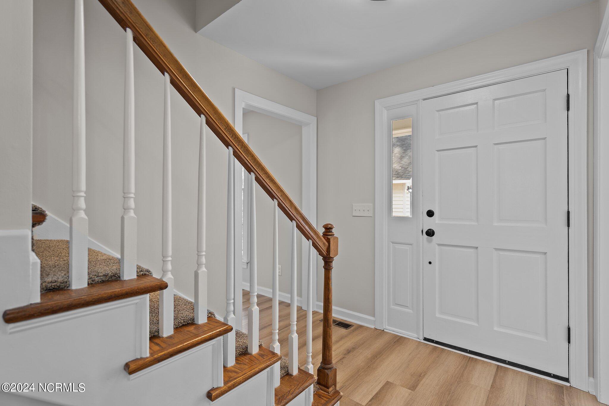 Entry foyer with a carpeted staircase, wood handrail, and white paneled front door.