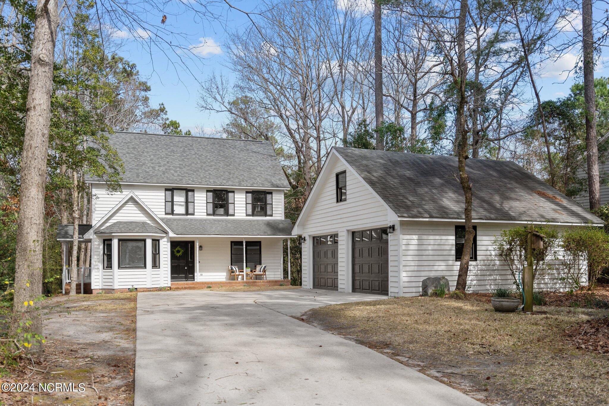 White two-story house with covered porch and detached two-car garage, framed by tall trees.