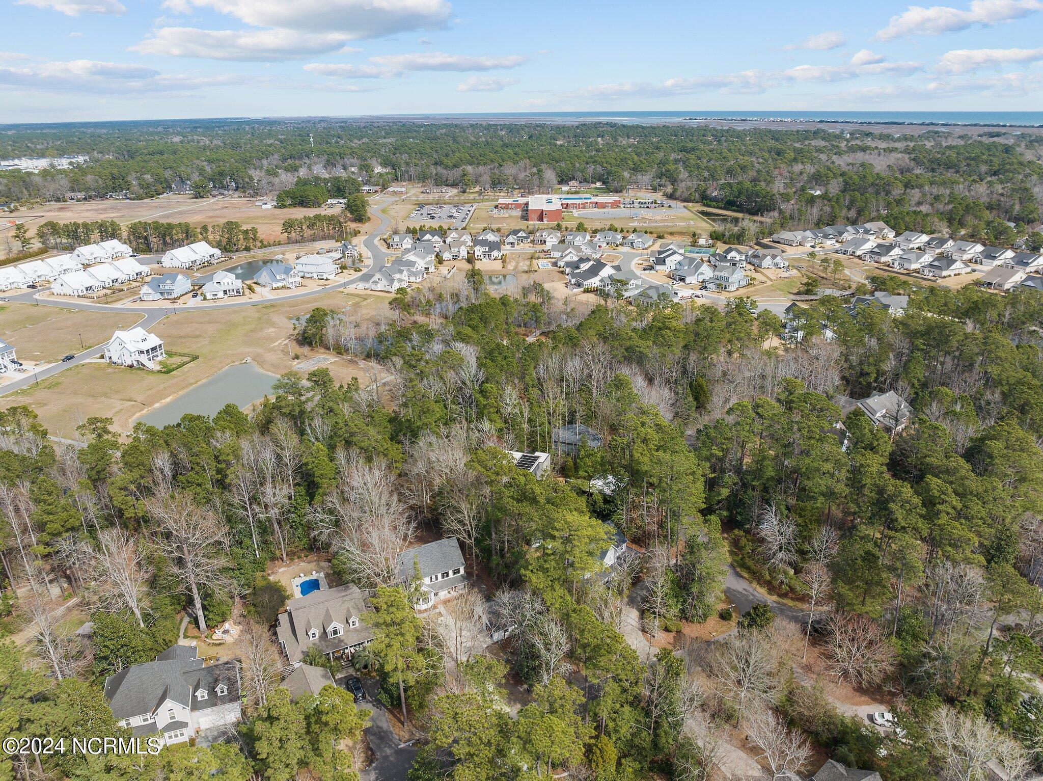 Aerial view of wooded homes and neighborhood, with a pond and coastline on the horizon.