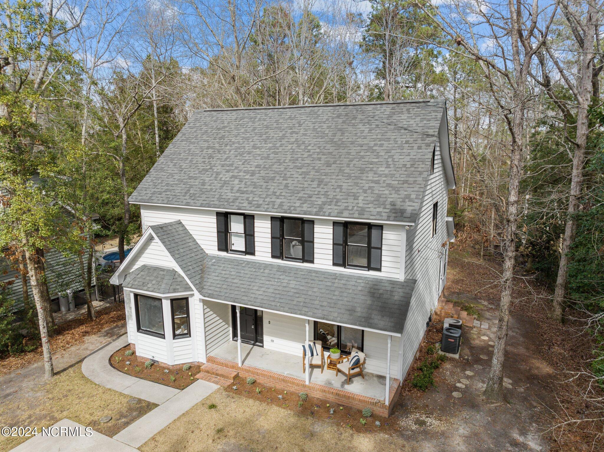 Two-story white house with black shutters, a covered porch, and a curved walkway, seen from above.