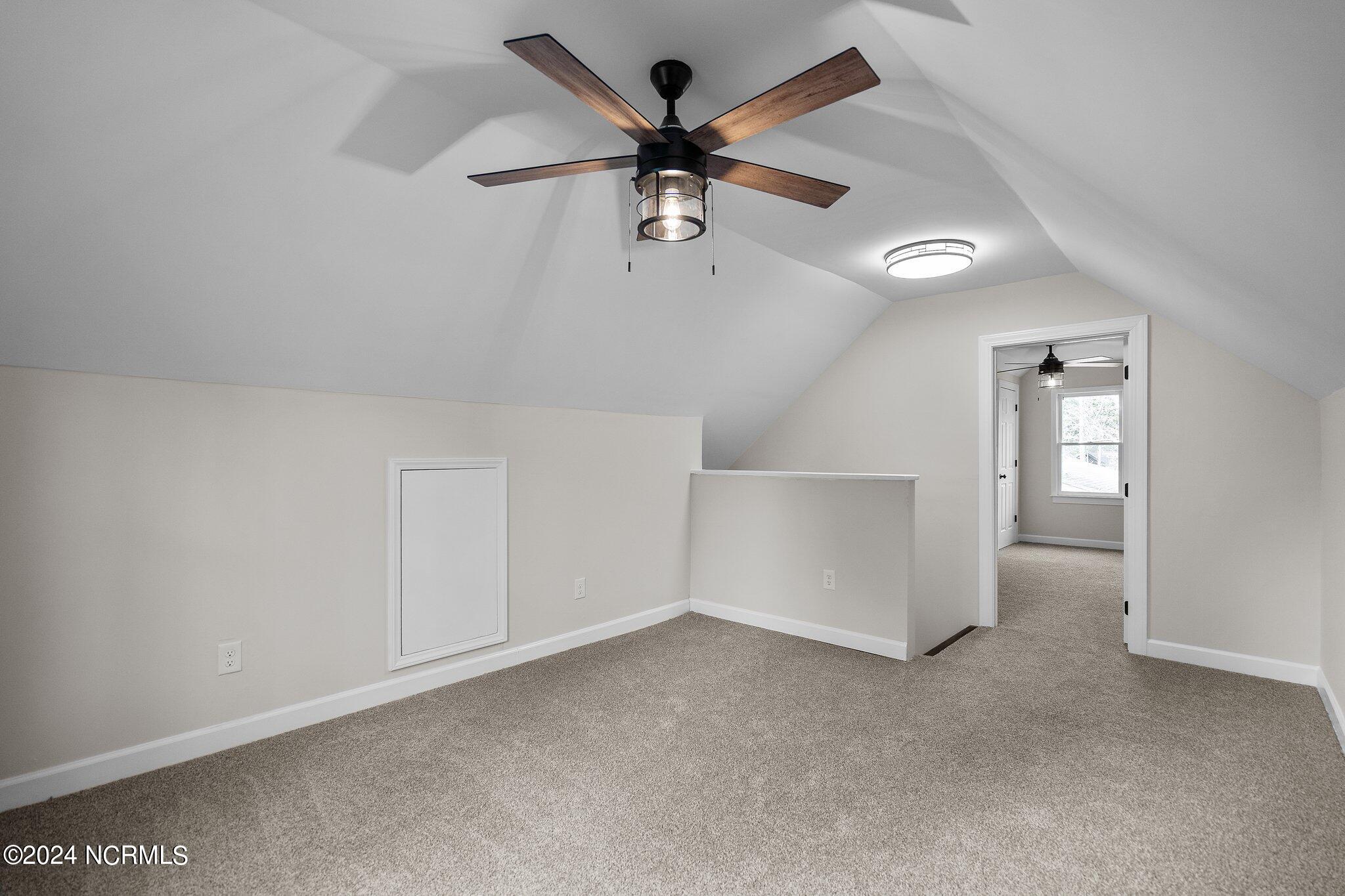 Carpeted upper-level room with a sloped ceiling, wood-blade ceiling fan, and doorway to an adjoining room.