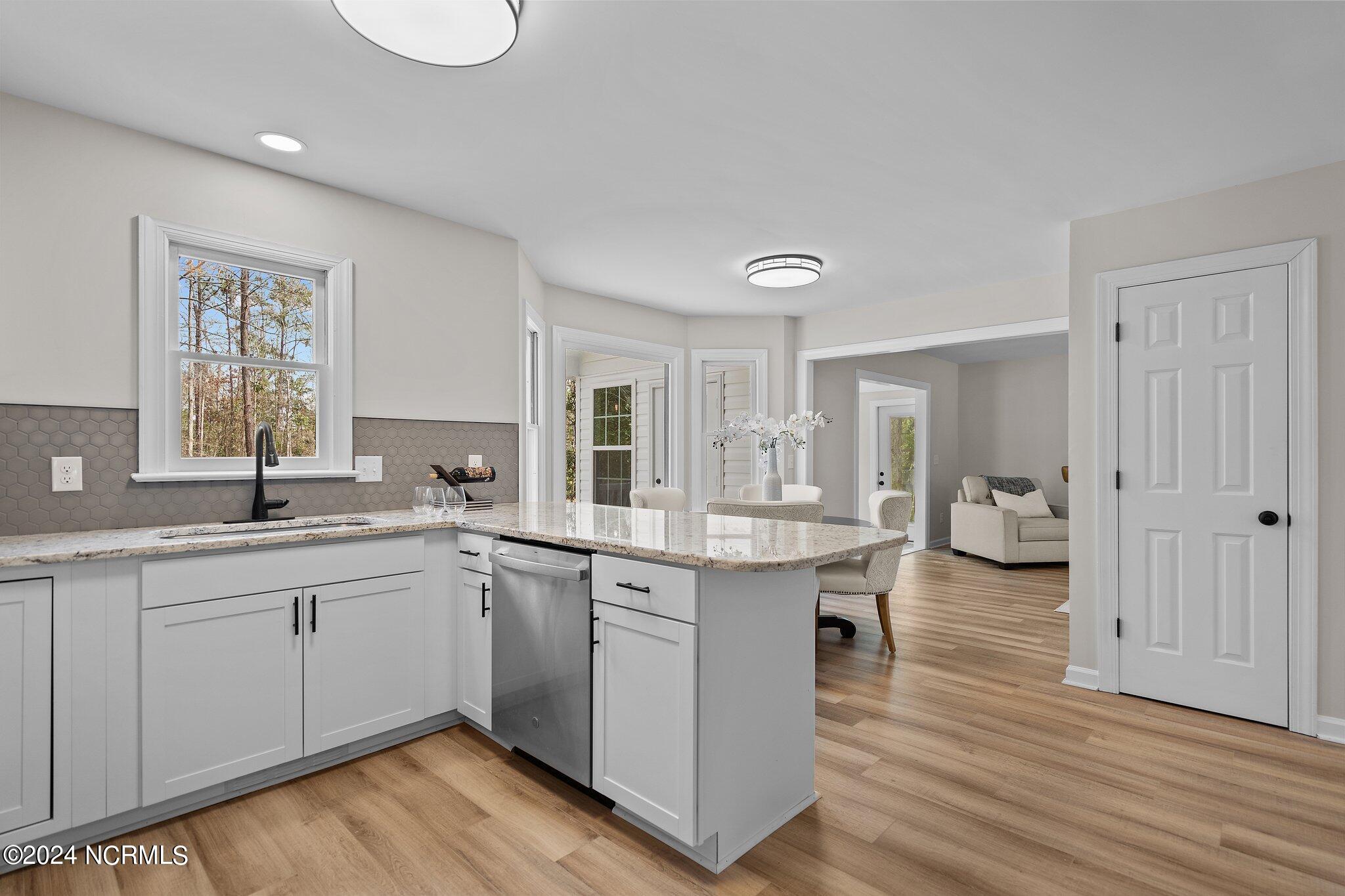 Bright white kitchen with a large quartz island opening to a dining area and living room.