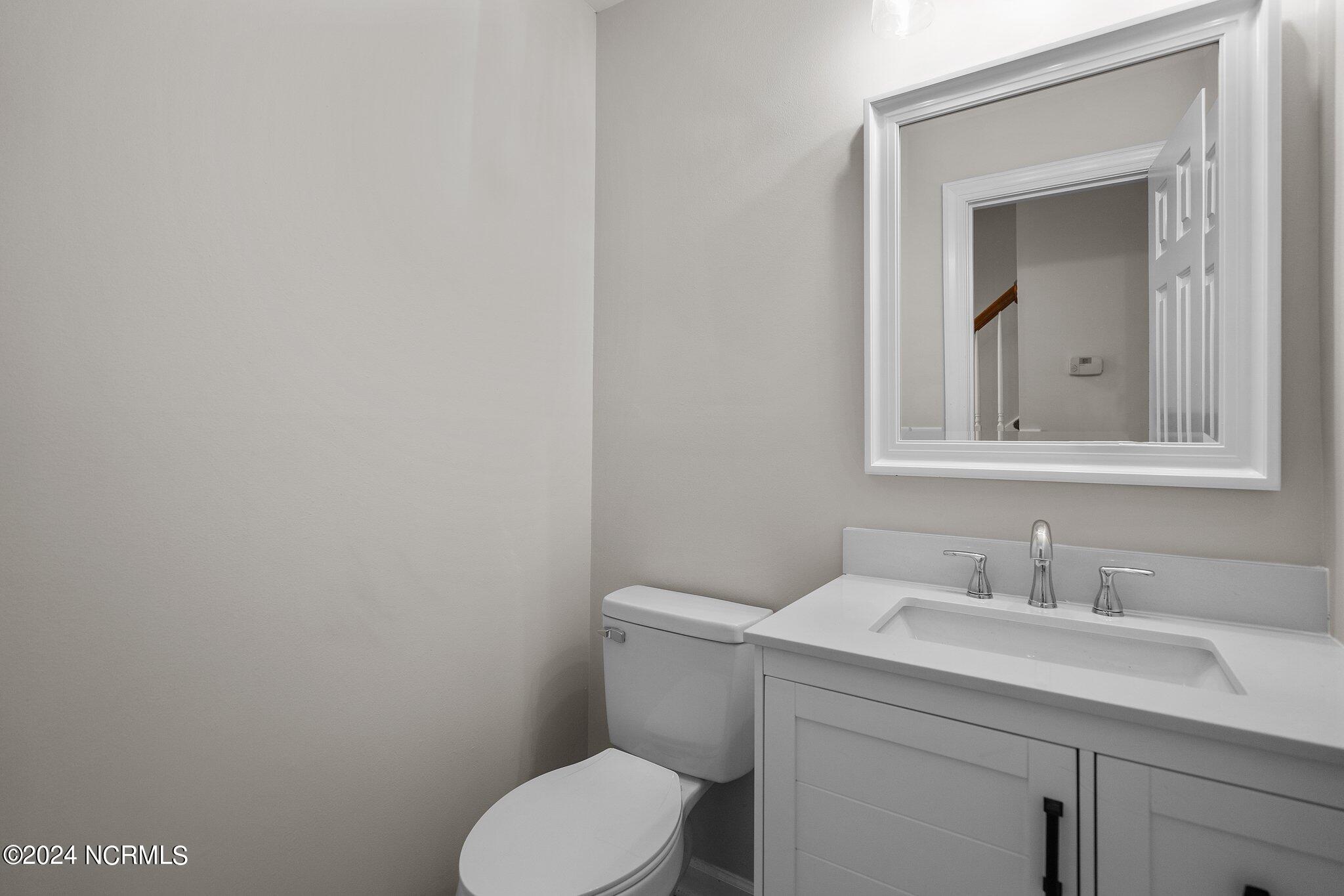 Bathroom with a white vanity, chrome fixtures, and a large framed mirror beside the toilet.