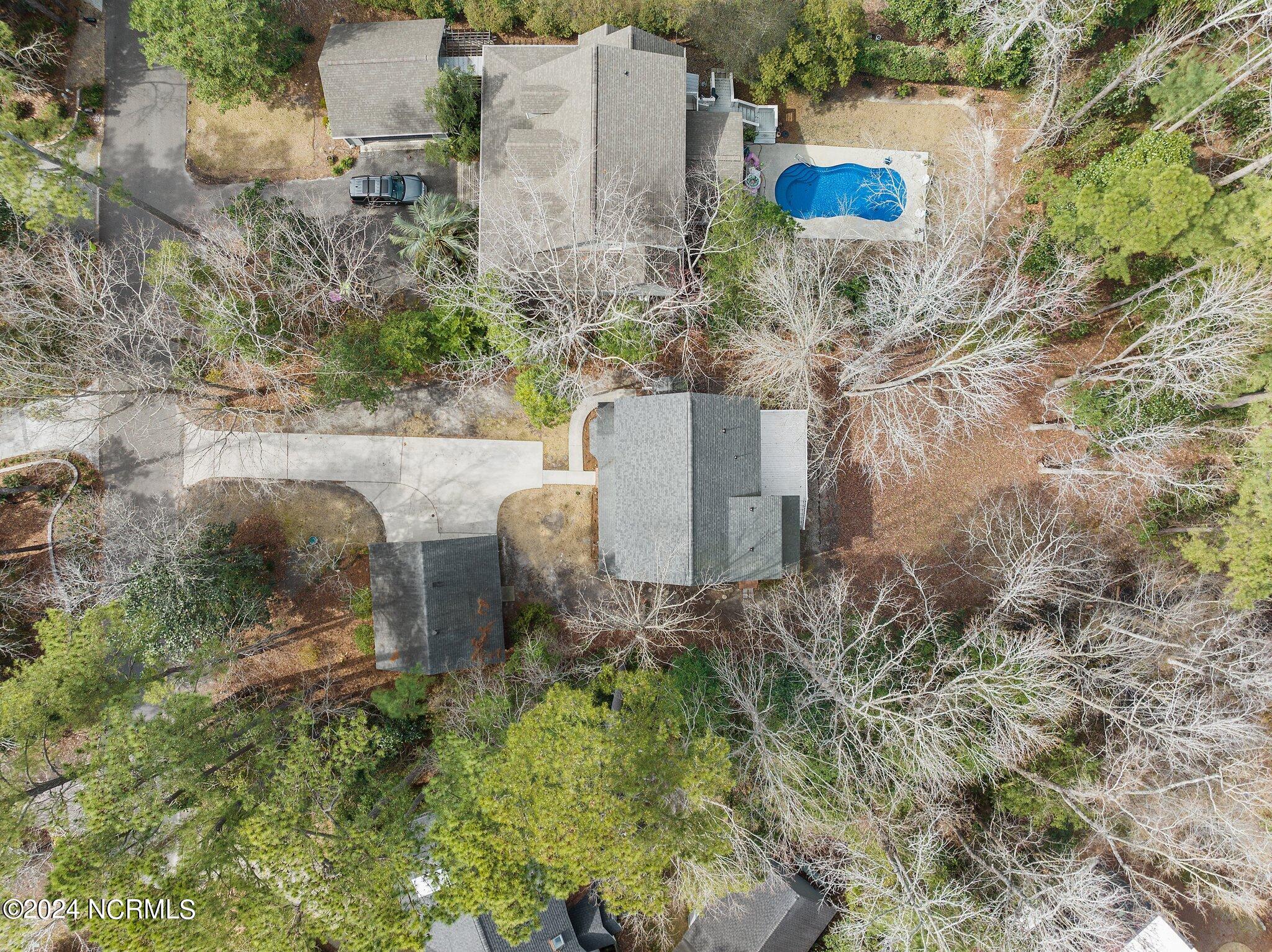 Aerial view of a wooded home with a blue pool and paved driveway.