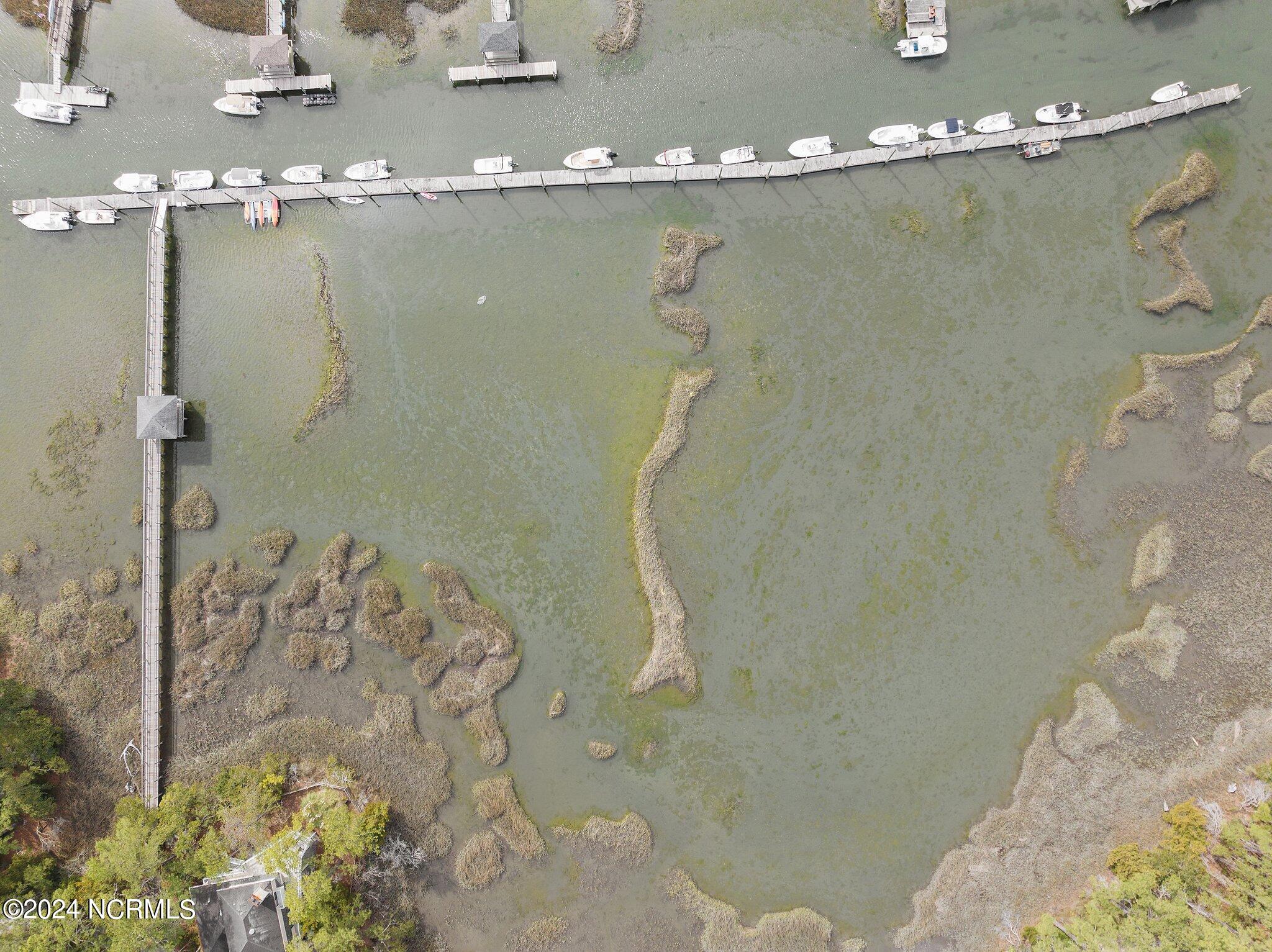 Aerial view of a creek marina with a long boat-lined dock and marshy shoreline.