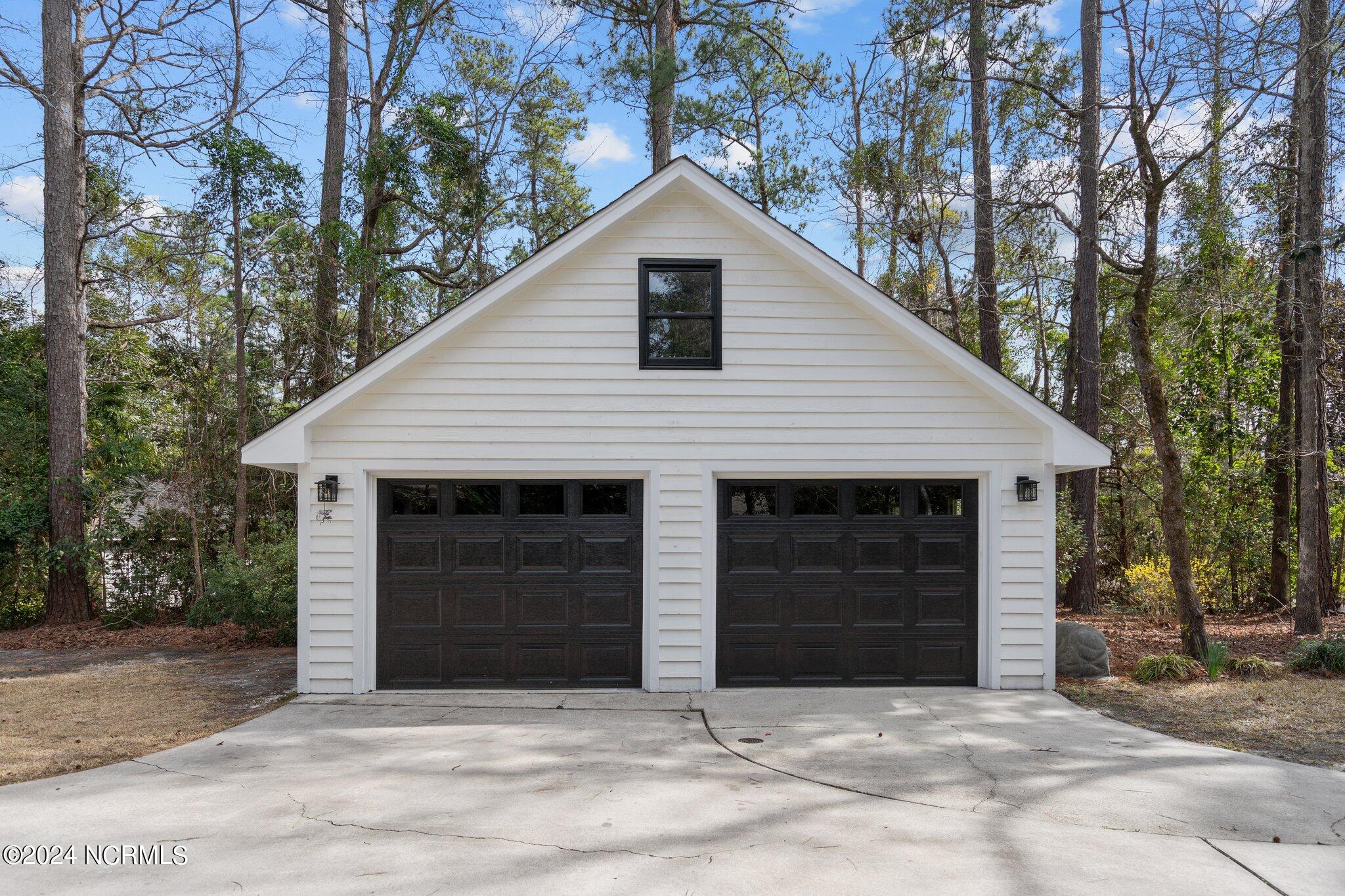 White detached garage with two black doors and an upper window, surrounded by trees.