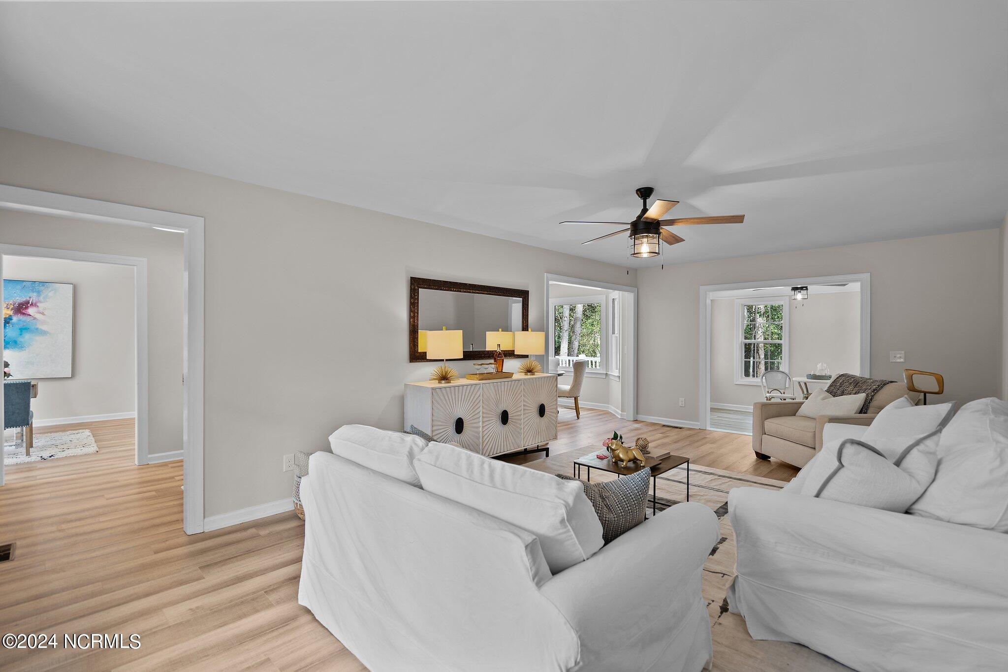 Staged living room with white sofas, light wood floors, and a console beneath a large mirror.