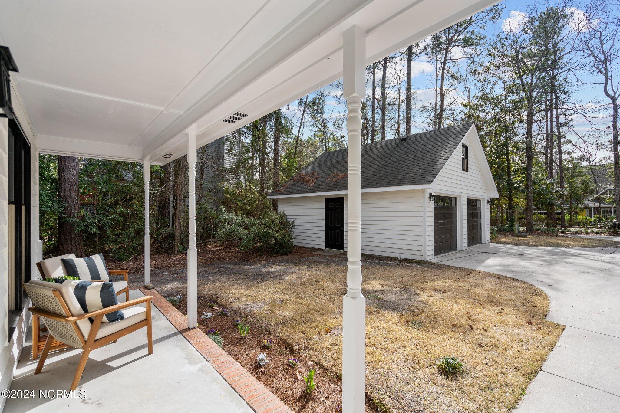 Covered porch with cushioned chairs beside a detached white garage and curved driveway.