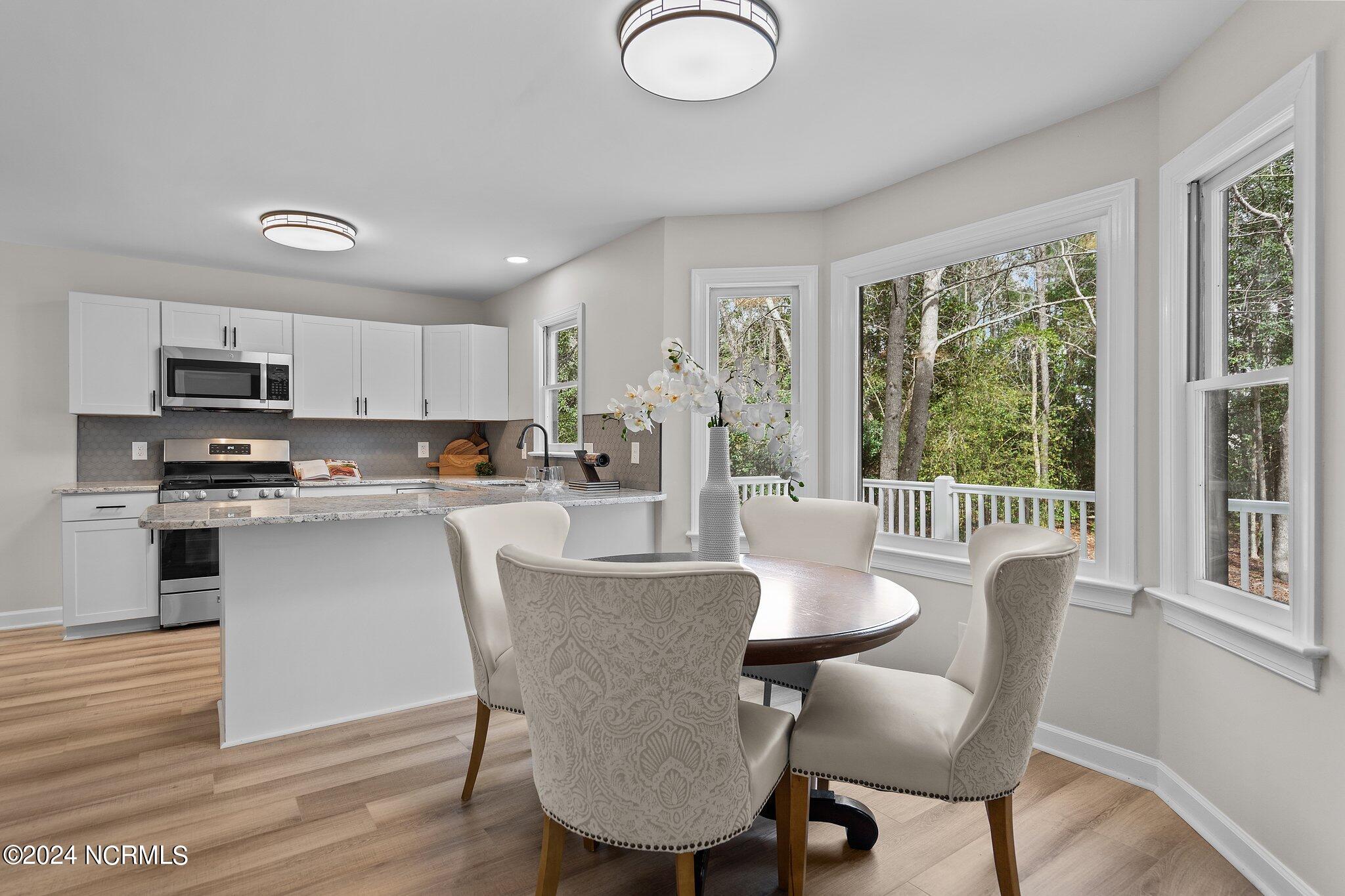 Kitchen and dining area with white cabinets, a round table, and large windows overlooking trees.