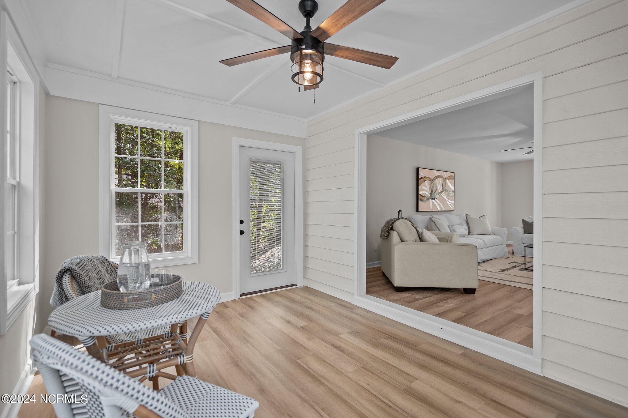 Furnished sunroom with wicker seating, a ceiling fan, and a wide opening to the living room.