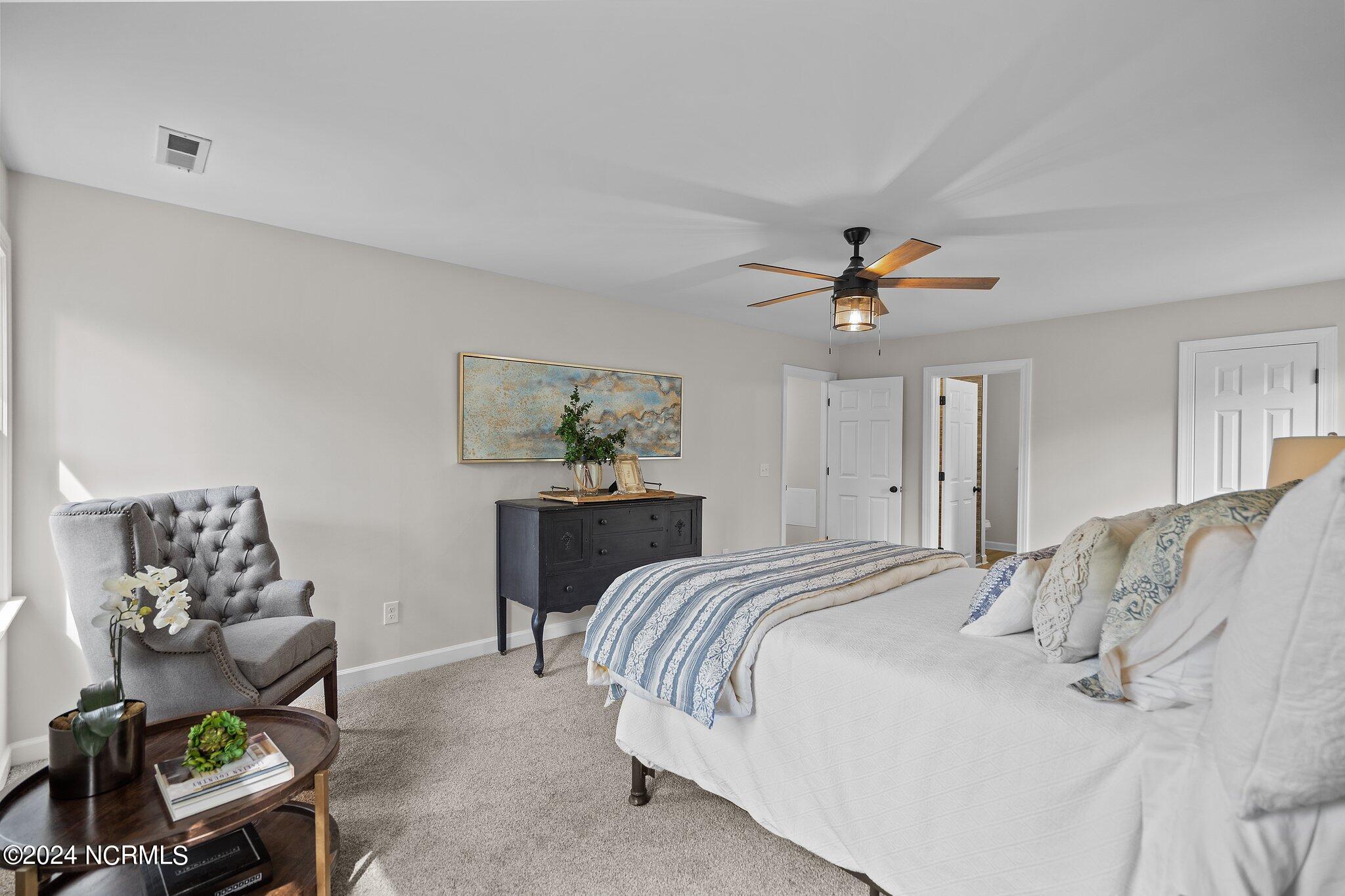 Staged bedroom with a white bed, blue-and-white bedding, gray armchair, and dark dresser.