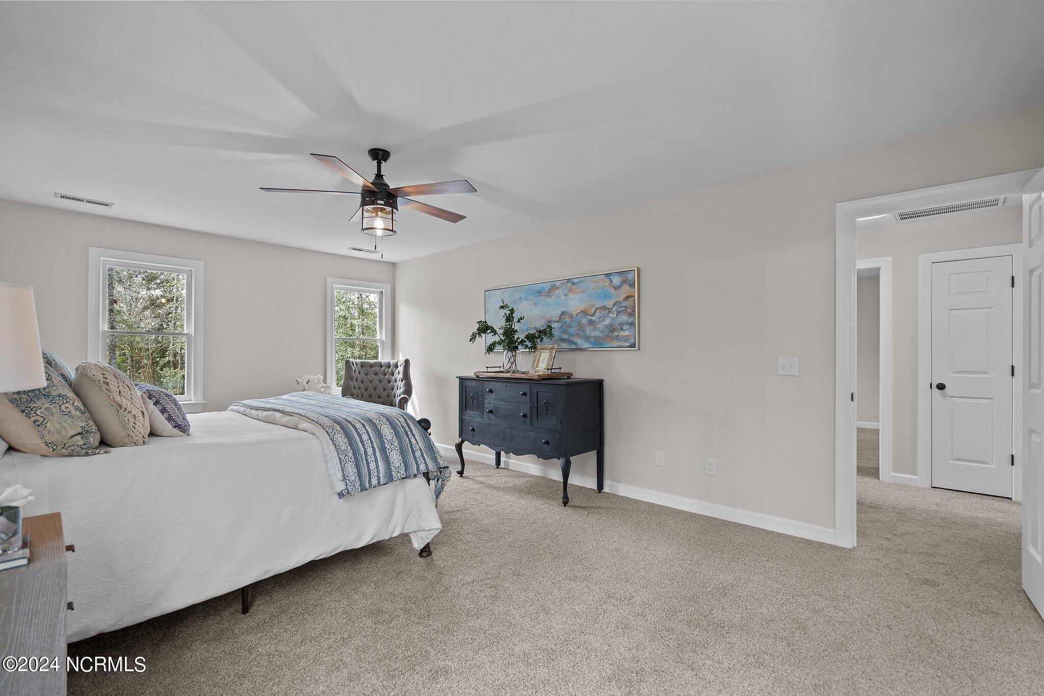 Furnished bedroom with blue patterned bedding, two windows, and a dark dresser beneath abstract wall art.