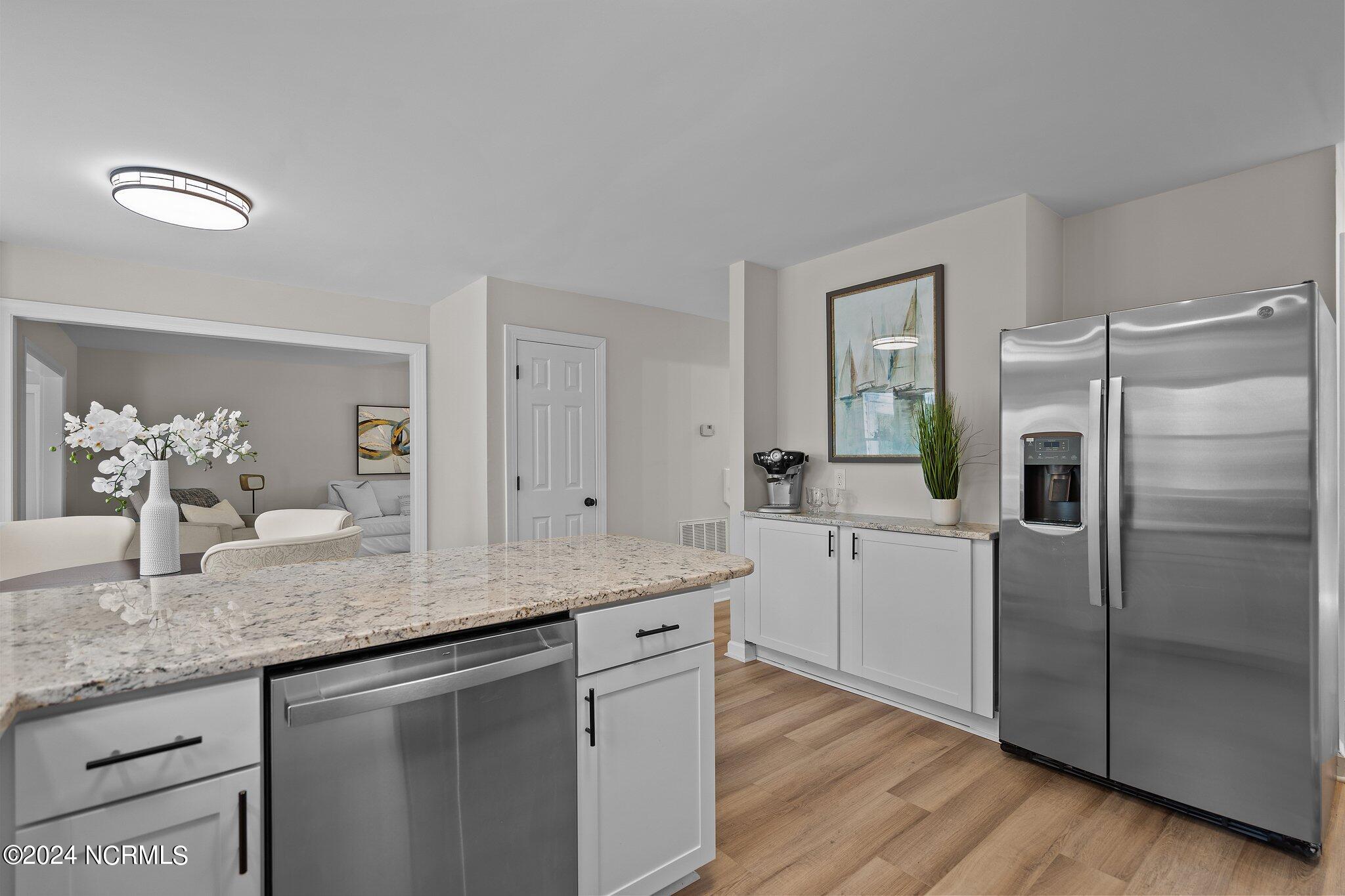 Kitchen with a granite island, stainless steel appliances, white cabinetry, and wood-look floors.