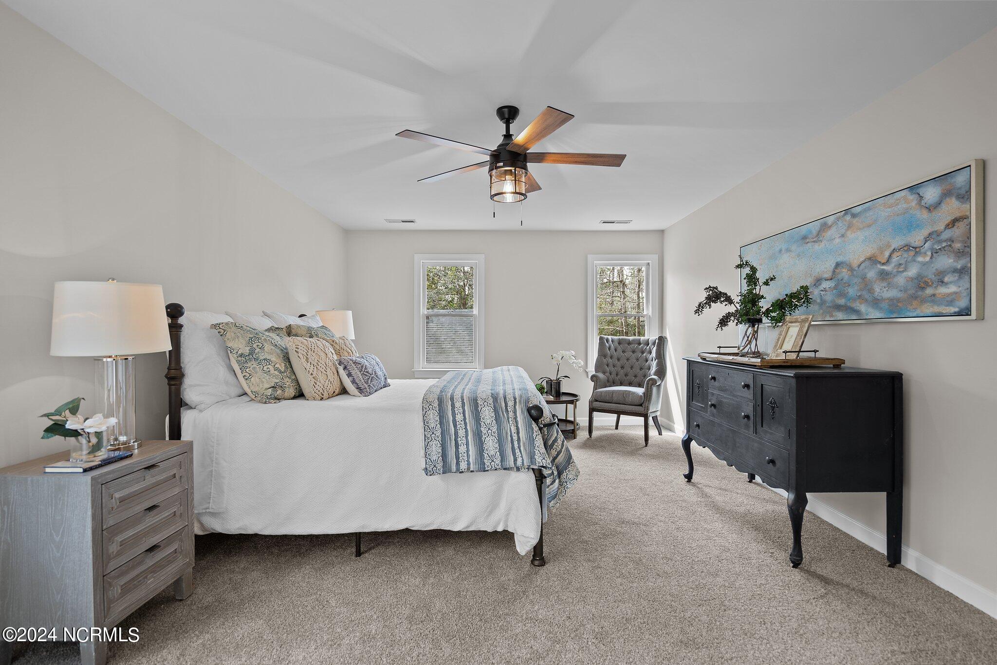 Staged bedroom with a white bed, blue patterned bedding, tray ceiling, and dark dresser.