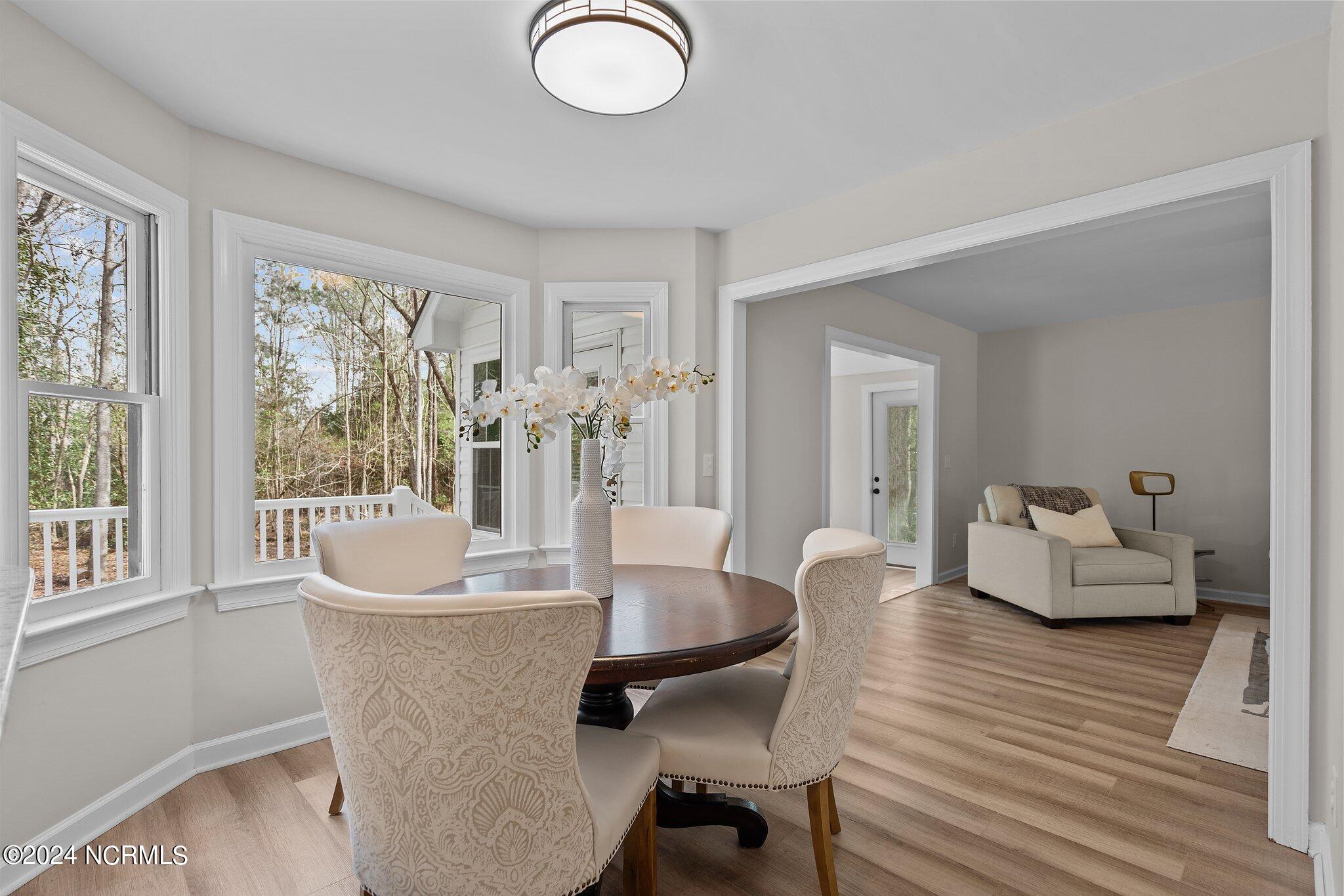 Dining room with a round table and patterned chairs beside large windows, opening to a sitting area.