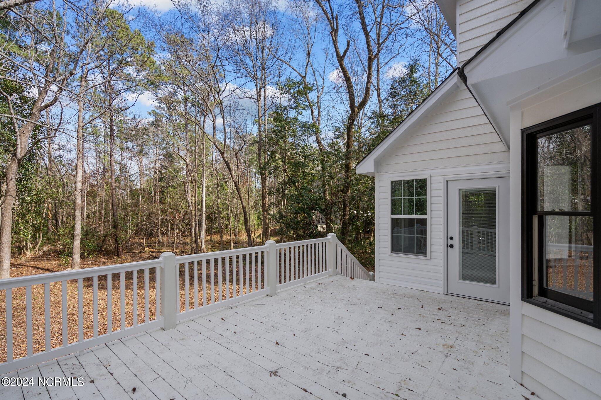 White wooden deck beside the home, overlooking a wooded backyard of mostly leafless trees.