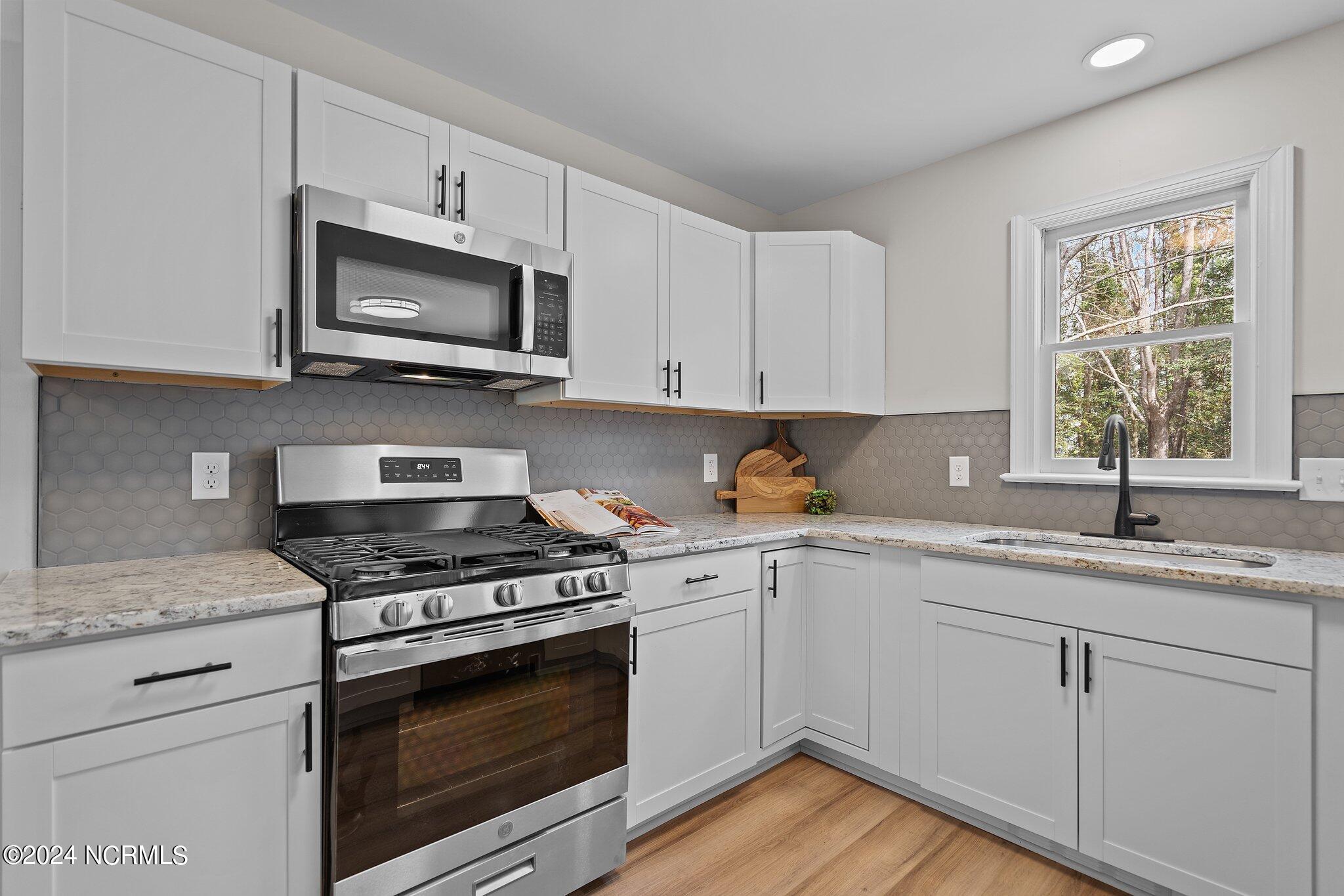 Kitchen with white shaker cabinets, gray hexagonal backsplash, stainless steel appliances, and a window over the sink.