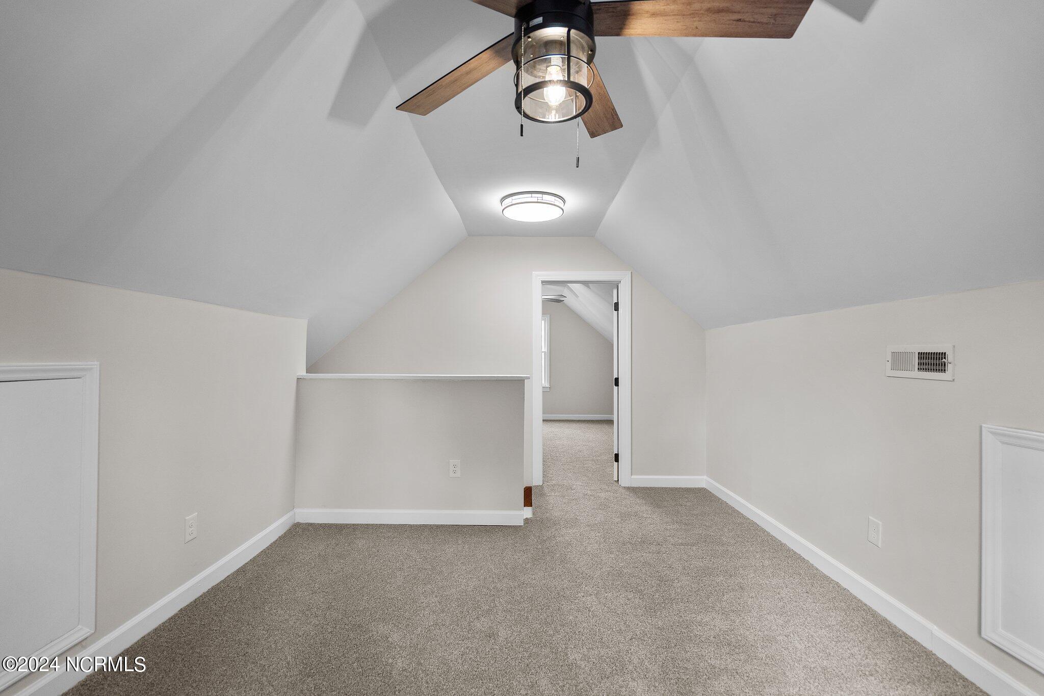 Carpeted upper-level room with sloped ceilings, a wood-blade ceiling fan, and an open doorway.