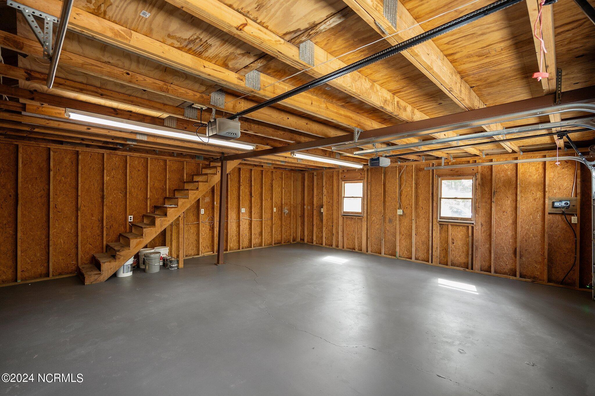 Unfinished garage with exposed wood framing, concrete floor, and stairs to a raised loft.