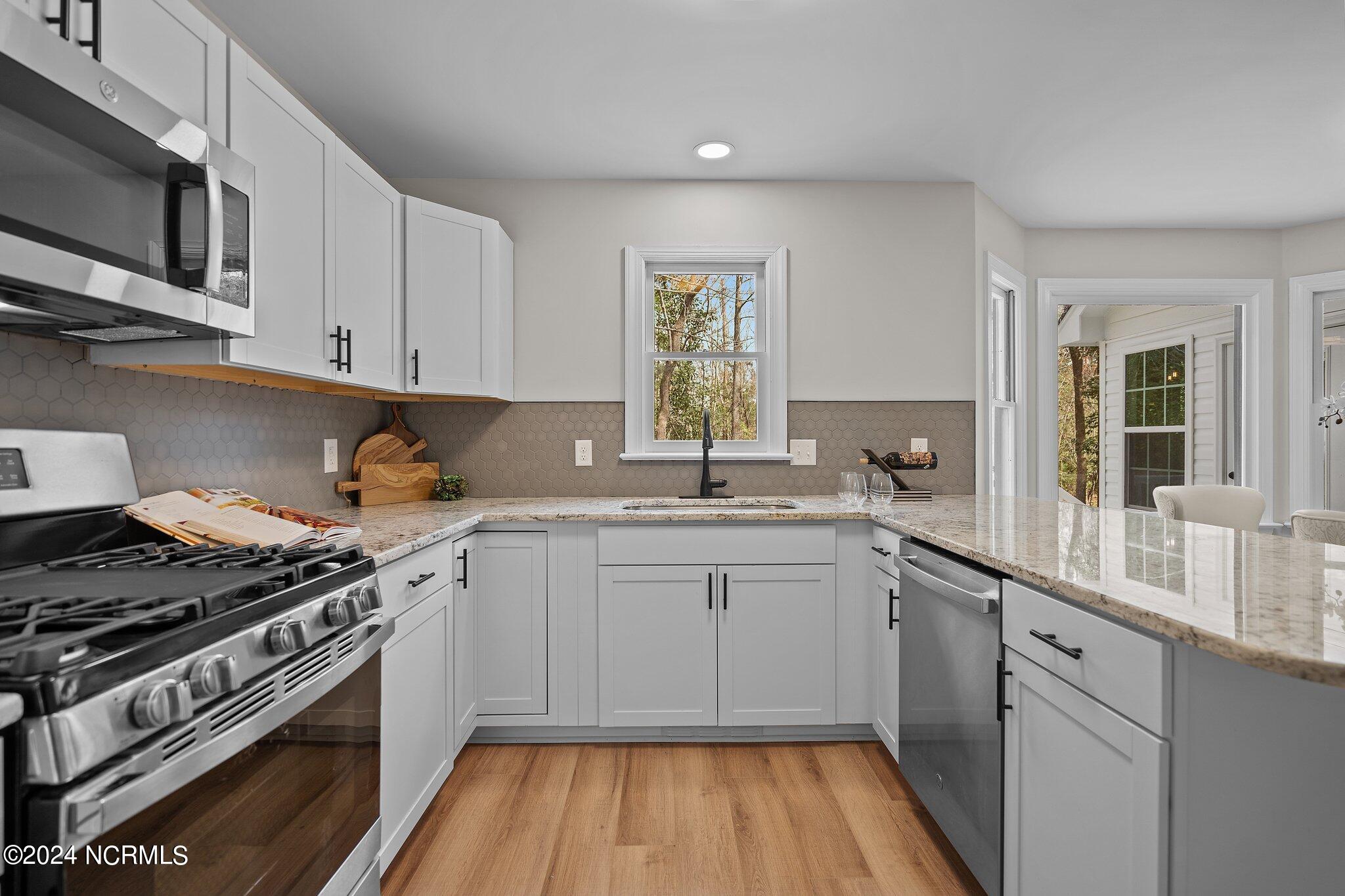 Kitchen with white shaker cabinets, gray hexagonal backsplash, granite counters, and stainless steel appliances.