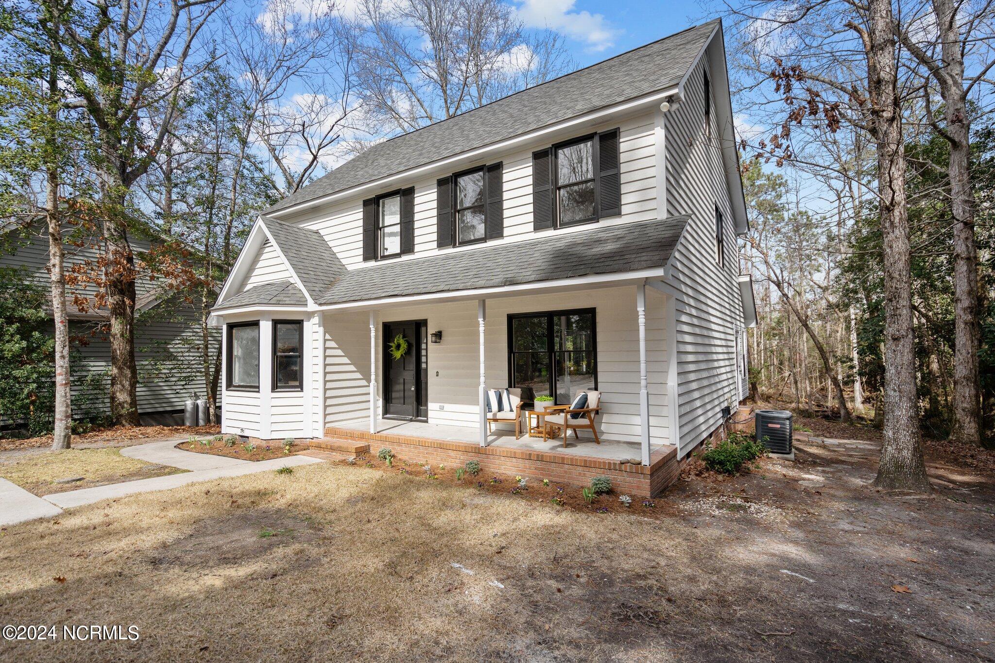 White two-story house with black shutters and a furnished covered porch among leafless trees.