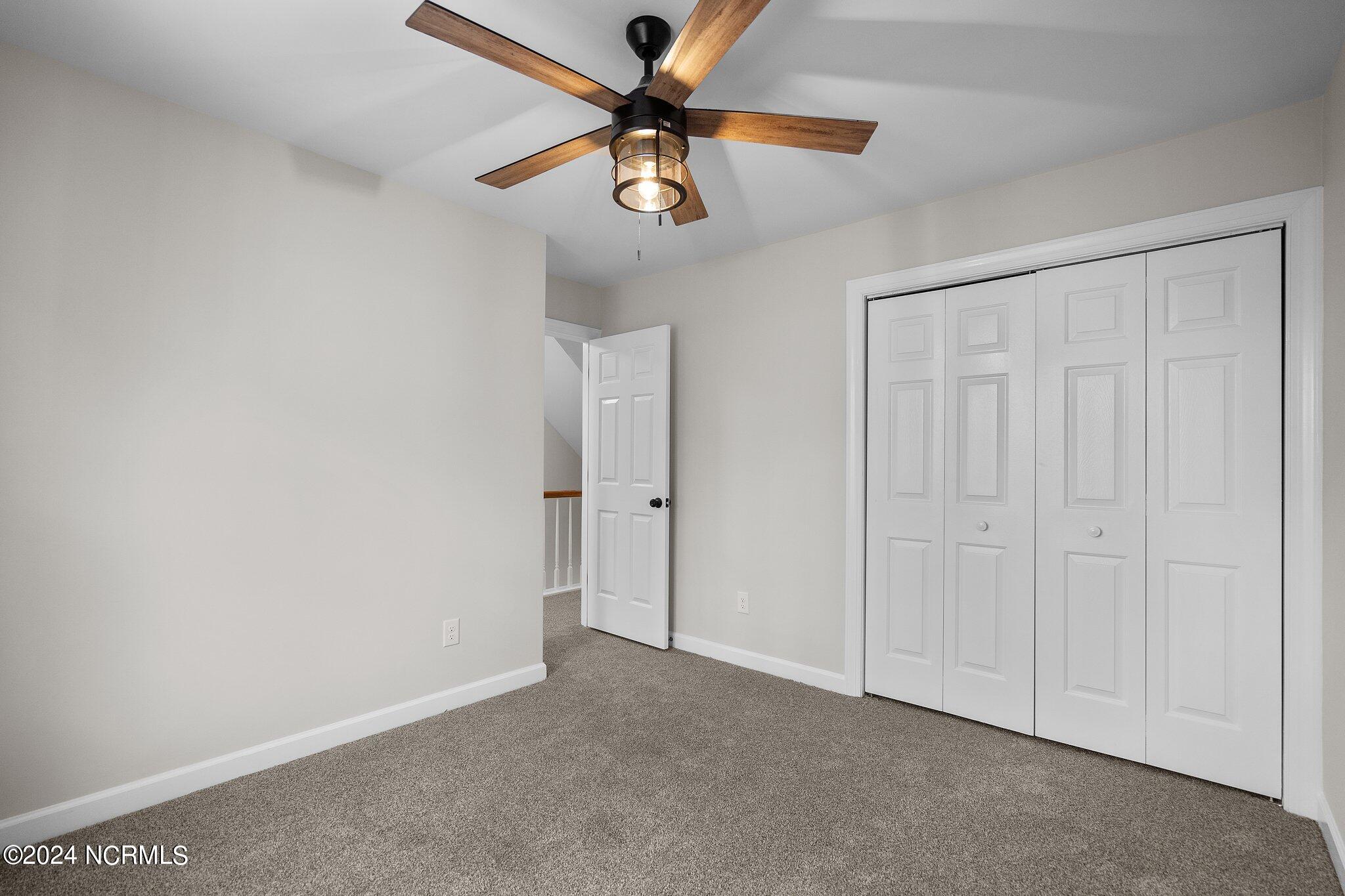 Empty bedroom with gray carpet, a wood-blade ceiling fan, and white folding closet doors.