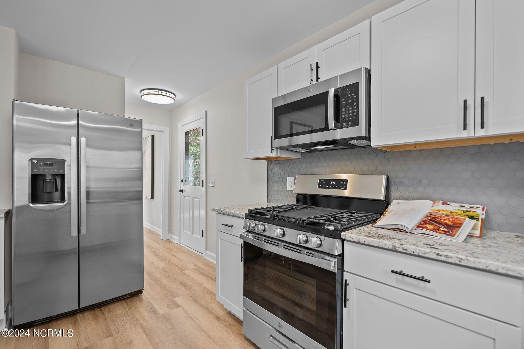 Modern kitchen with white cabinets, stainless steel appliances, and a gray hexagonal tile backsplash.