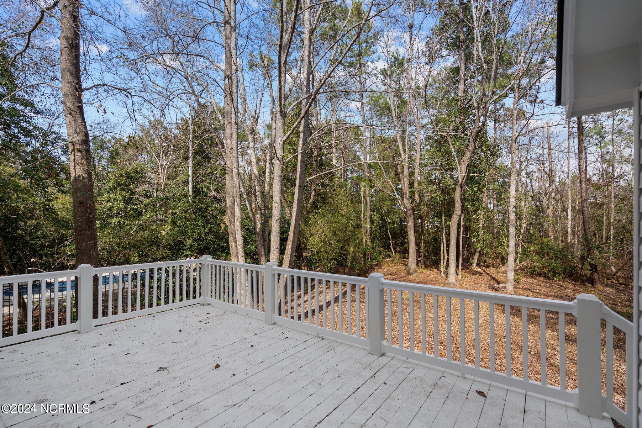 White deck overlooking a wooded backyard, with a glimpse of a swimming pool through the railing.