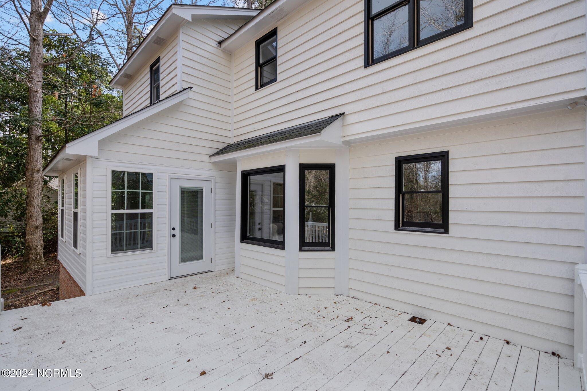 White two-story house viewed from a broad wooden deck, with black-framed windows and trees nearby.