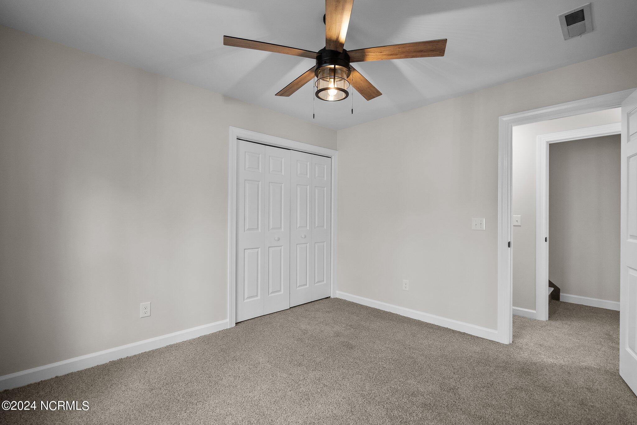 Empty carpeted bedroom with a double-door closet and wood-blade ceiling fan.