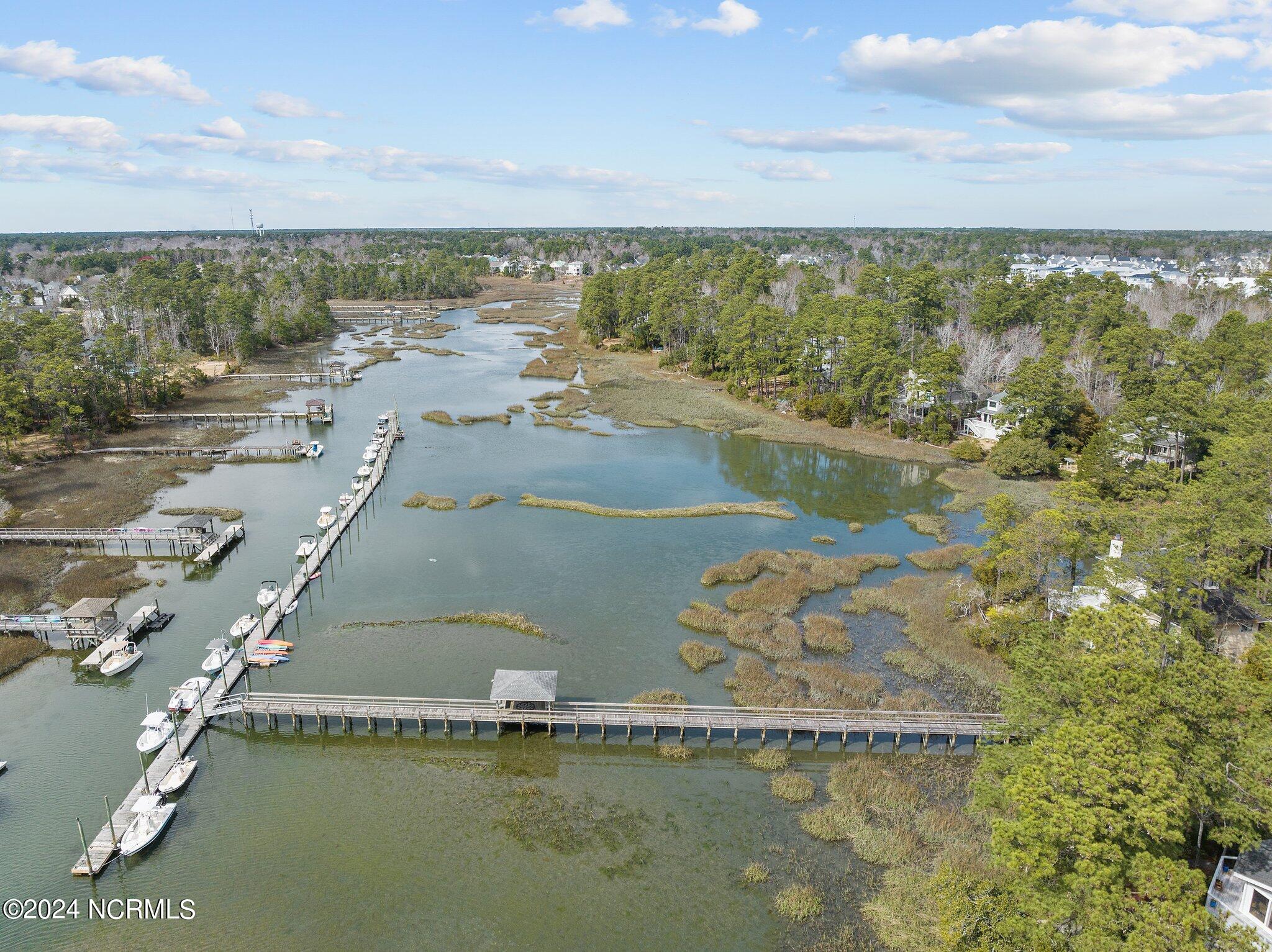 Aerial view of a marsh-lined creek with boats and long docks along wooded shores.