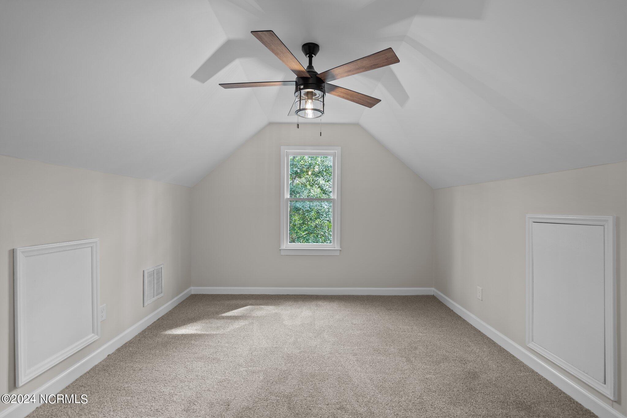 Empty carpeted room with a vaulted ceiling, ceiling fan, and centered window.