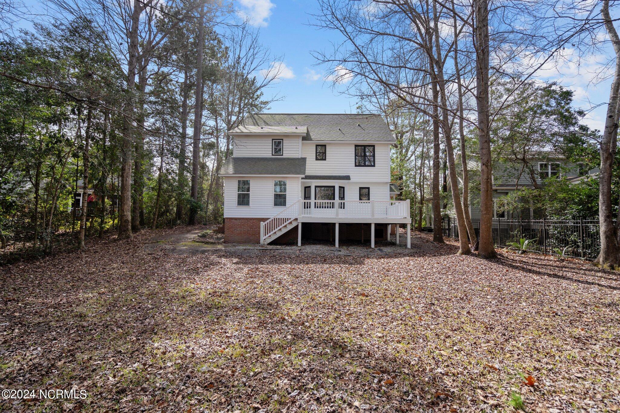 Two-story white house with a raised rear deck and stairs in a wooded, leaf-covered yard.