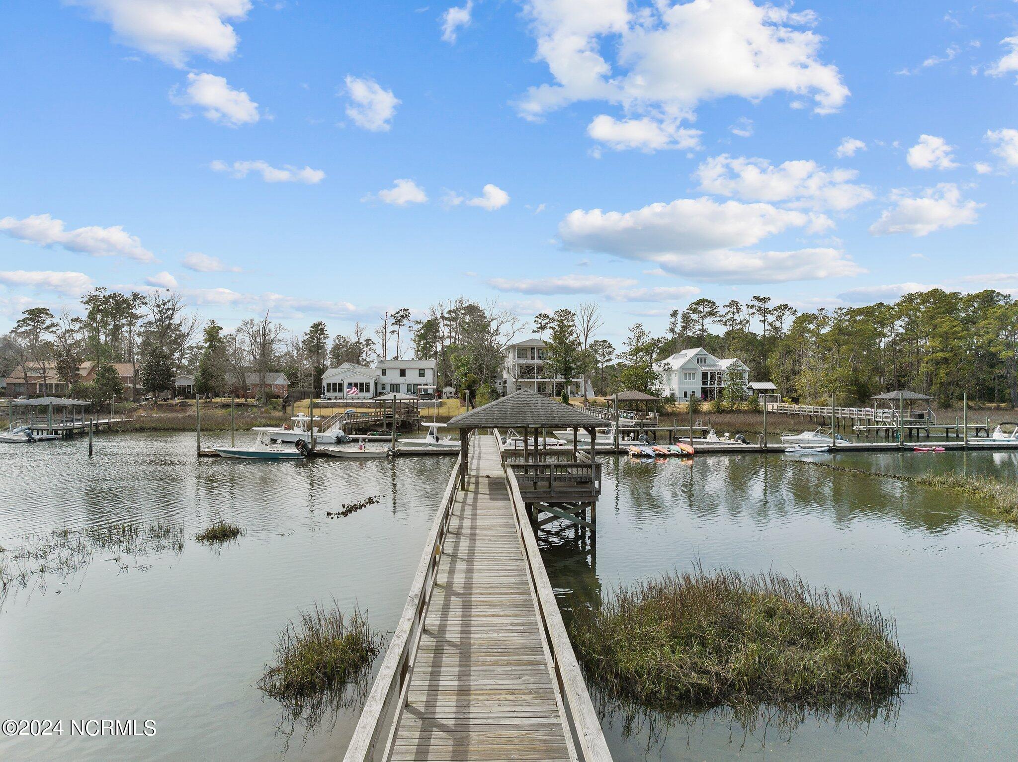 A wooden dock extends across the creek toward moored boats and waterfront homes.