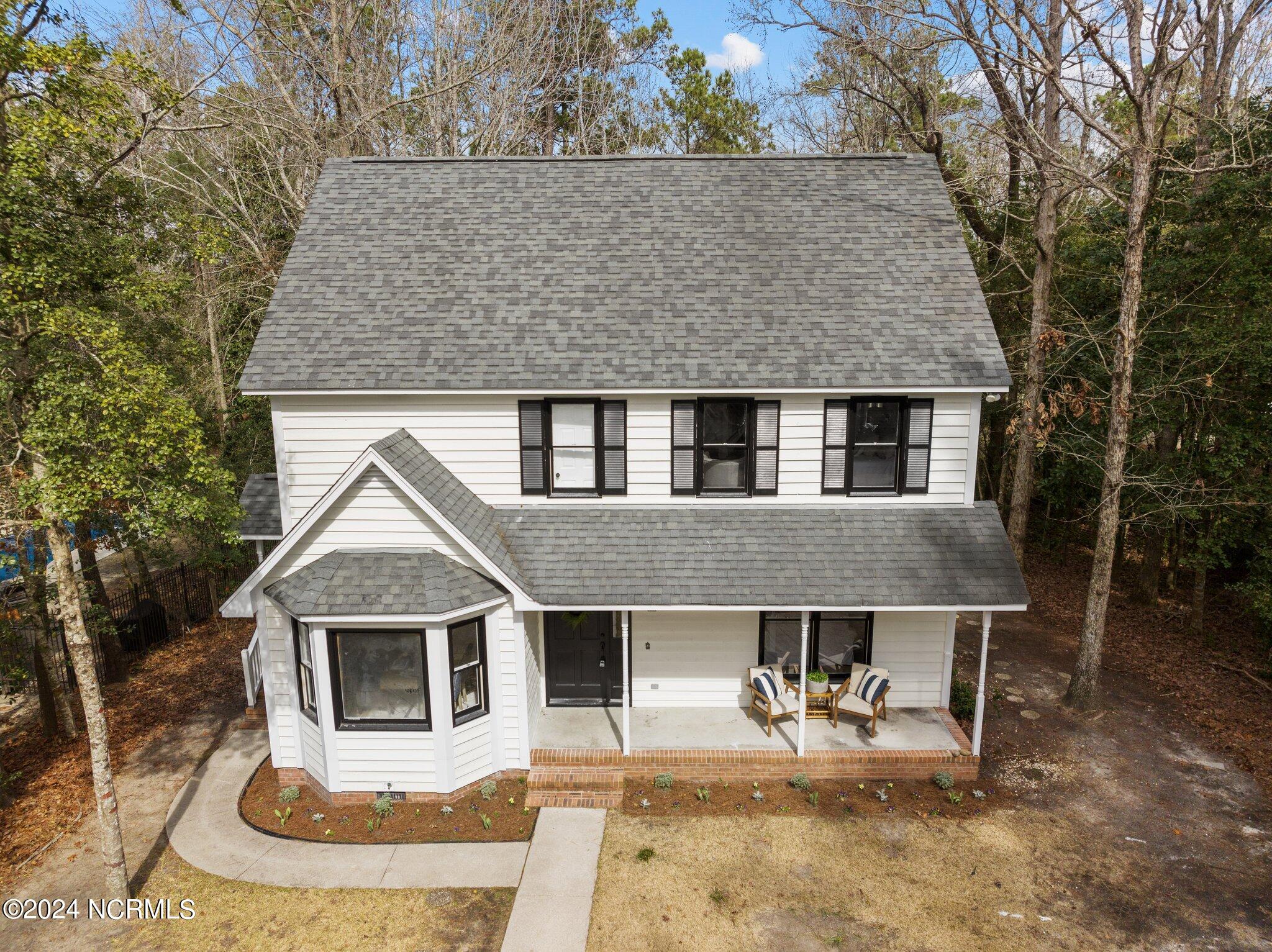 White two-story house with black shutters, a covered porch, and a curved front walkway.