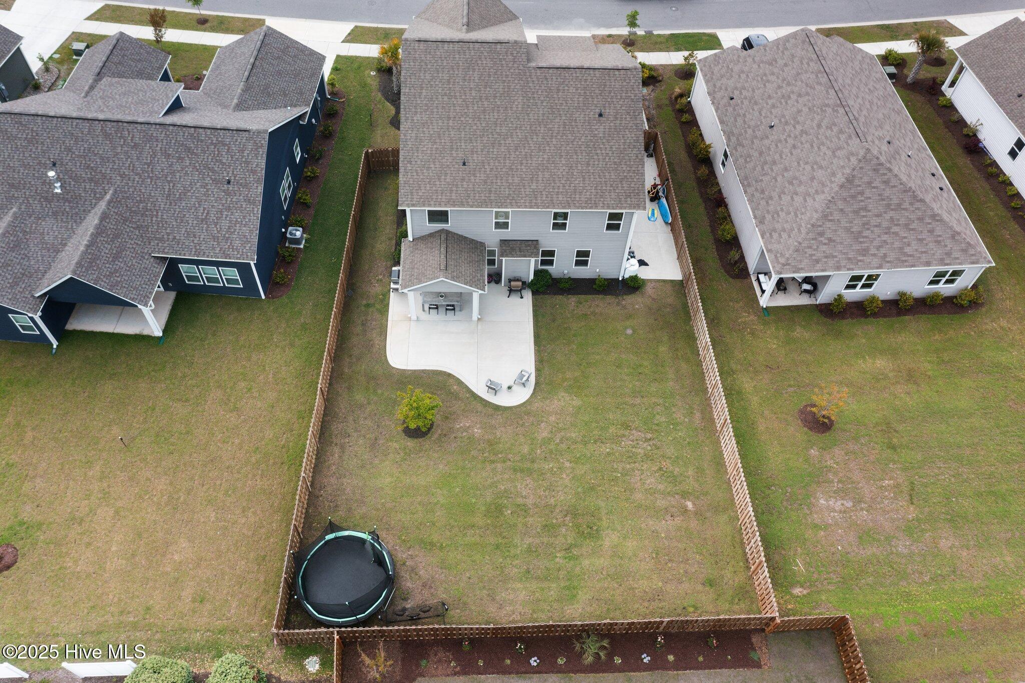Aerial view of a two-story home’s fenced backyard, with a large patio and trampoline.