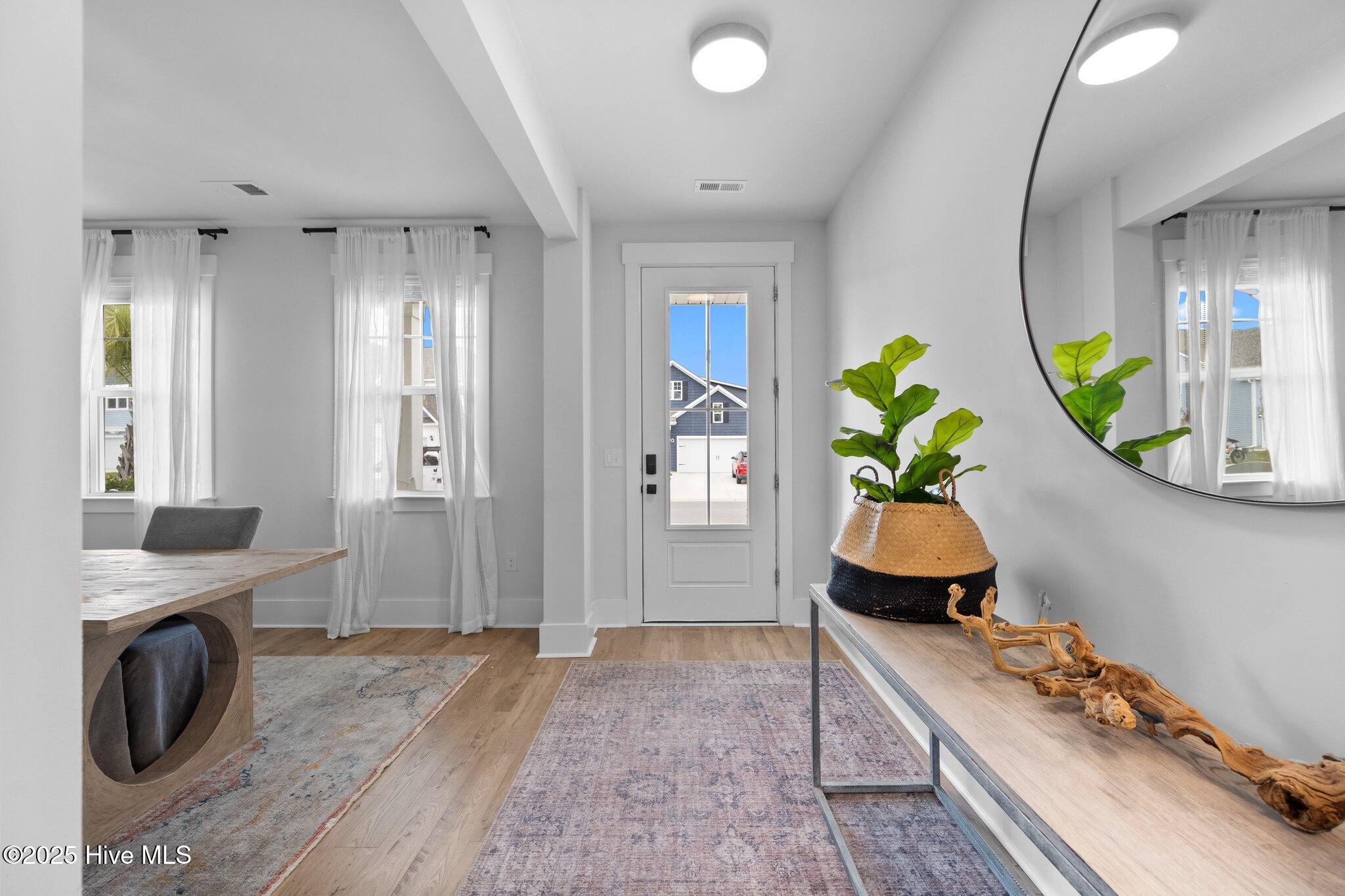 Bright entry foyer with glass-paneled front door, console table, round mirror, and potted plant.