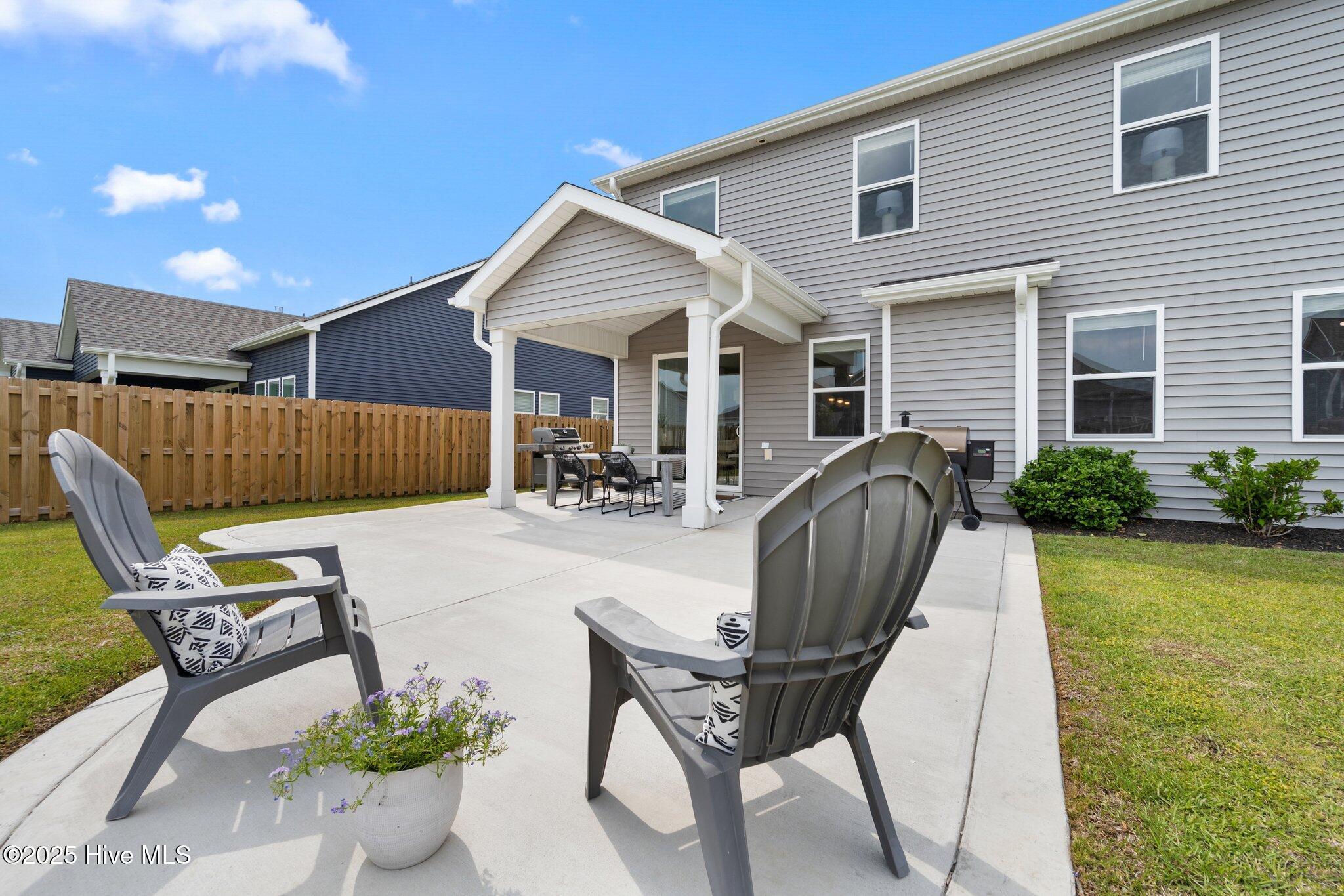 Backyard patio with Adirondack chairs, a covered porch, and a fenced lawn.
