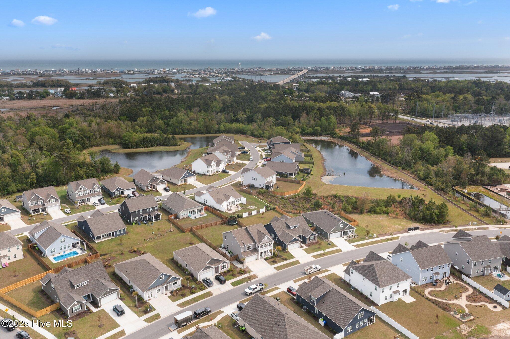 Aerial view of a coastal neighborhood with ponds, wooded areas, and the ocean beyond.