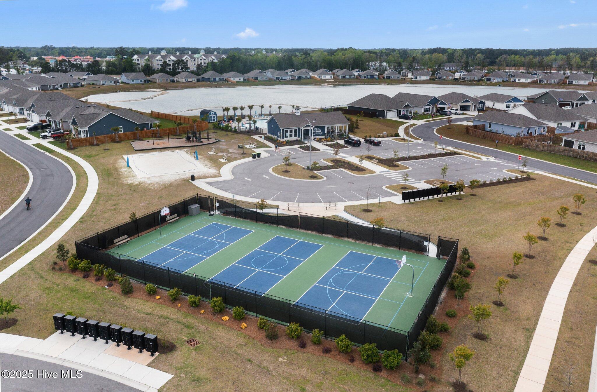 Aerial view of a residential community with three basketball courts, a sand volleyball court, and a pond.