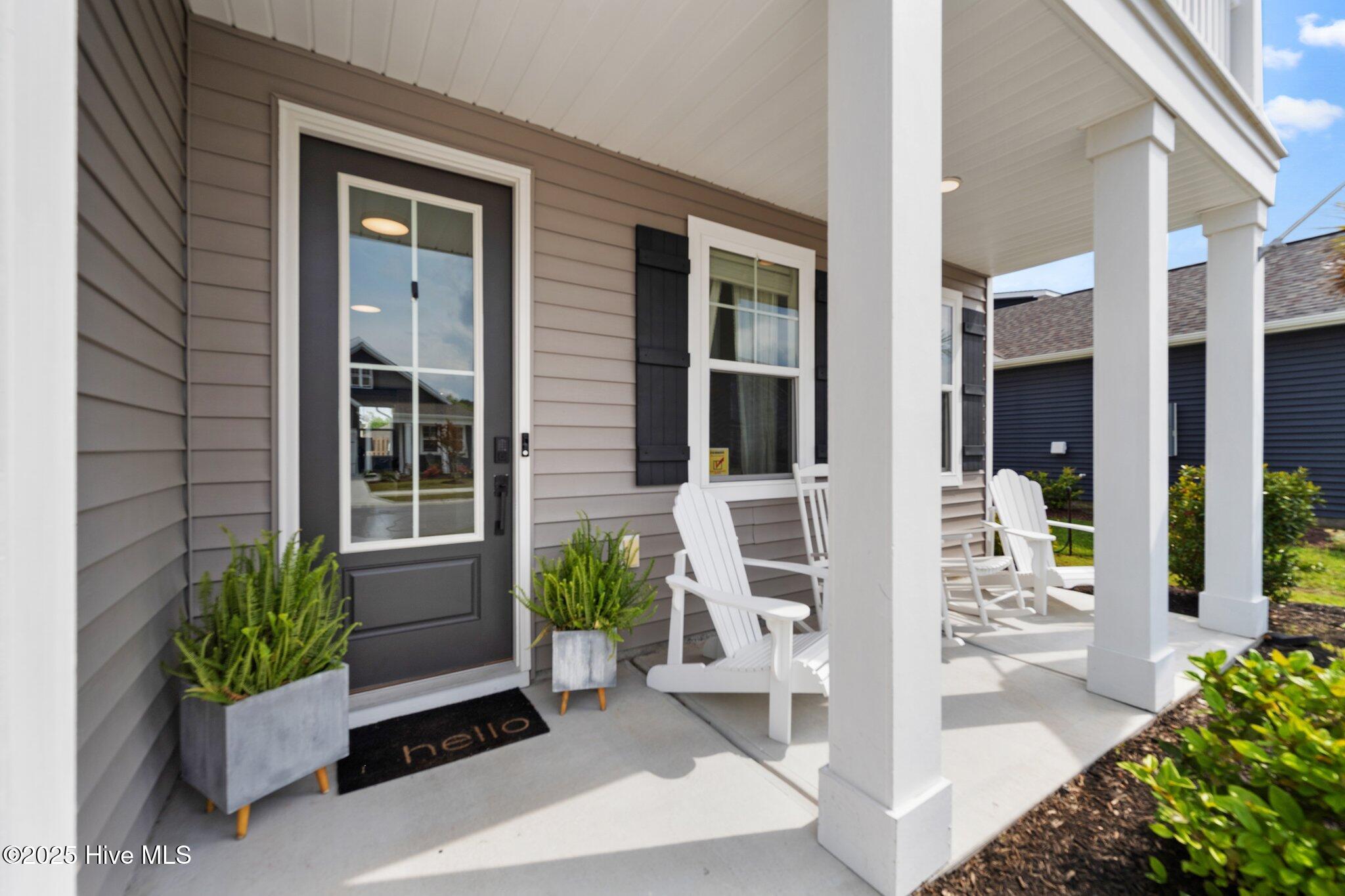 Home’s covered front porch with a dark entry door, white columns, potted plants, and Adirondack chairs.