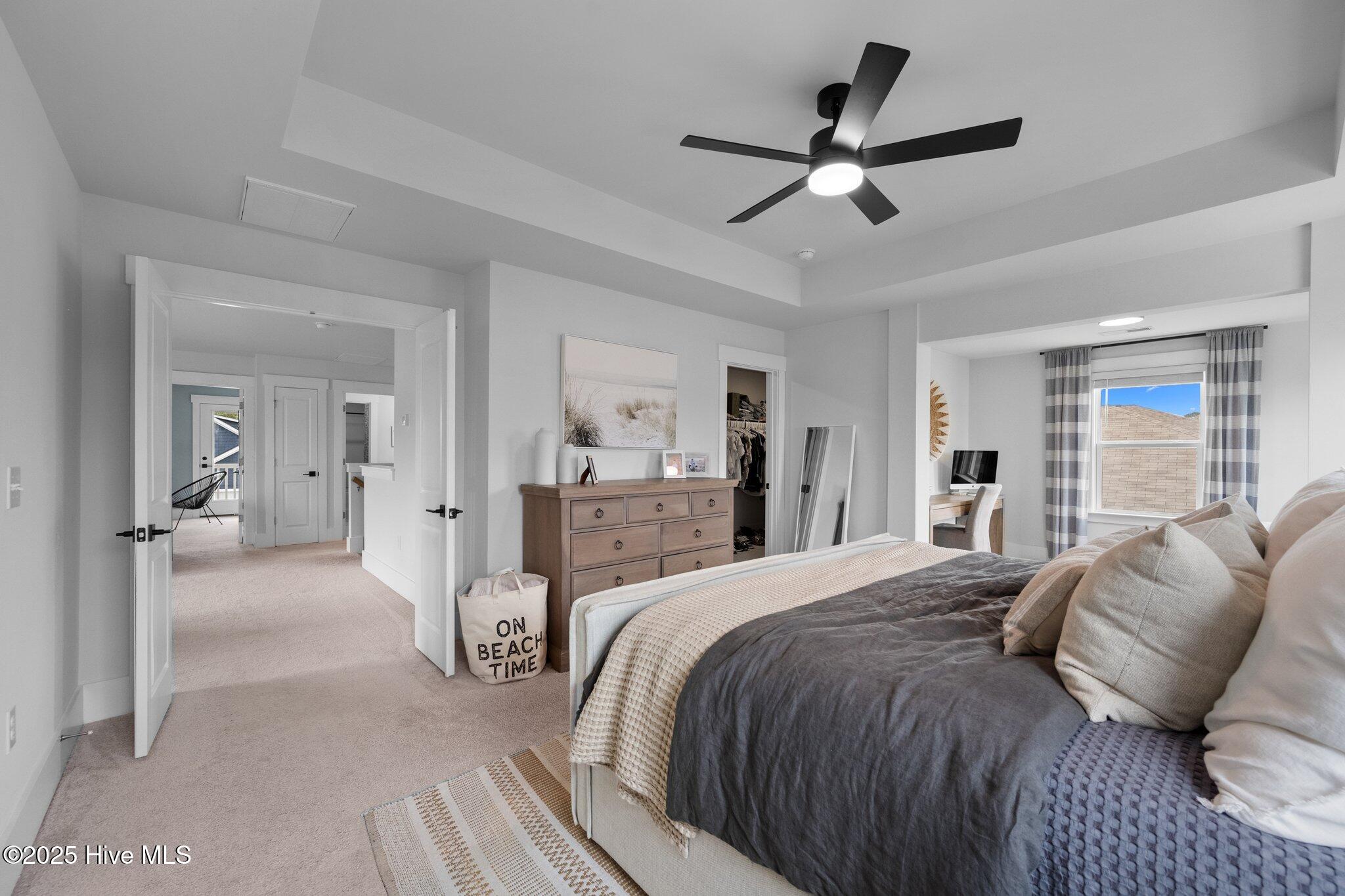Bedroom with a gray-and-cream bed, wood dresser, black ceiling fan, and adjoining desk area.