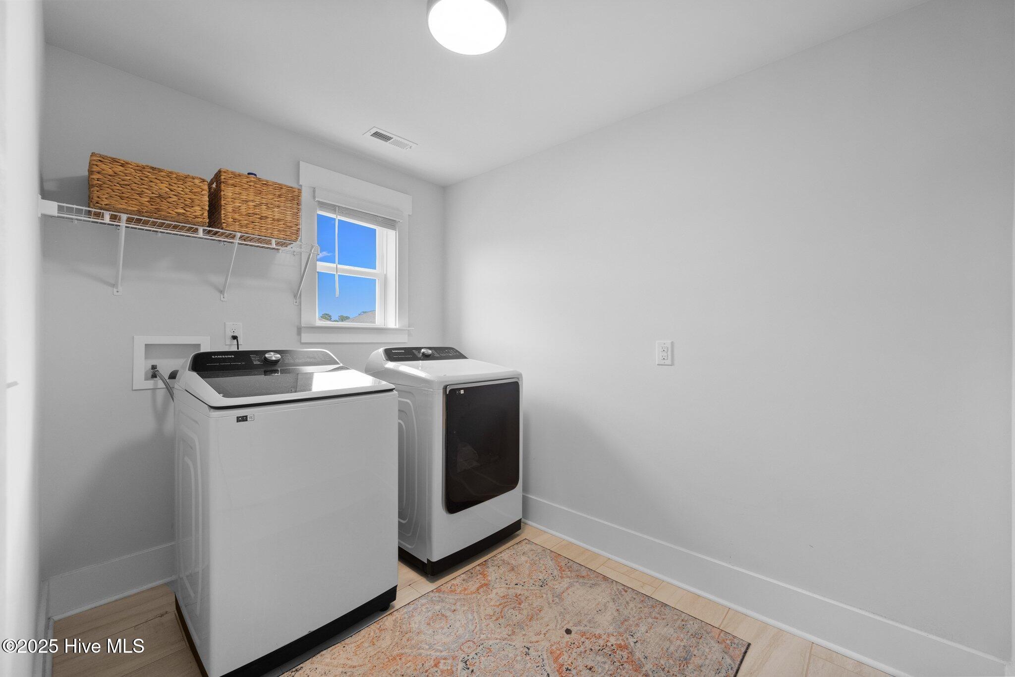 Laundry room with a white washer and dryer, woven baskets on a shelf, and a patterned rug.