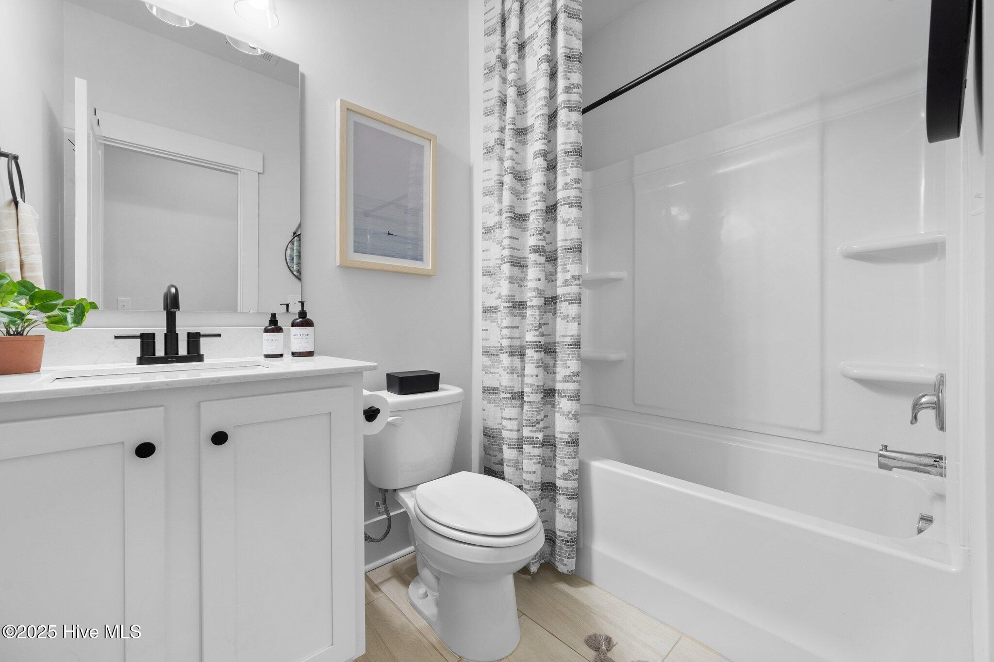 Bathroom with white vanity, toilet, and bathtub behind a patterned shower curtain.