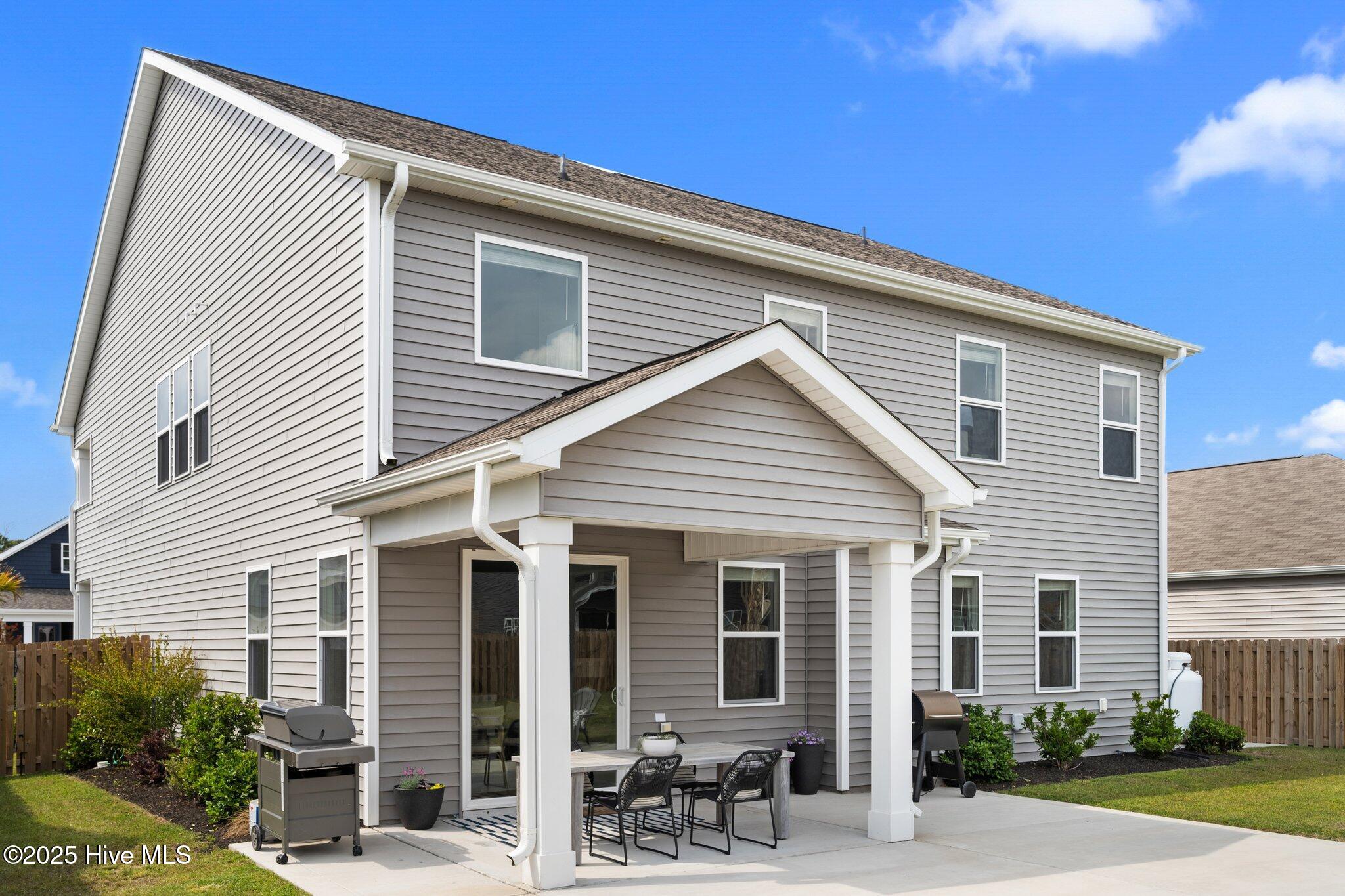 Rear of a two-story gray home with a covered patio, outdoor dining set, and two grills.